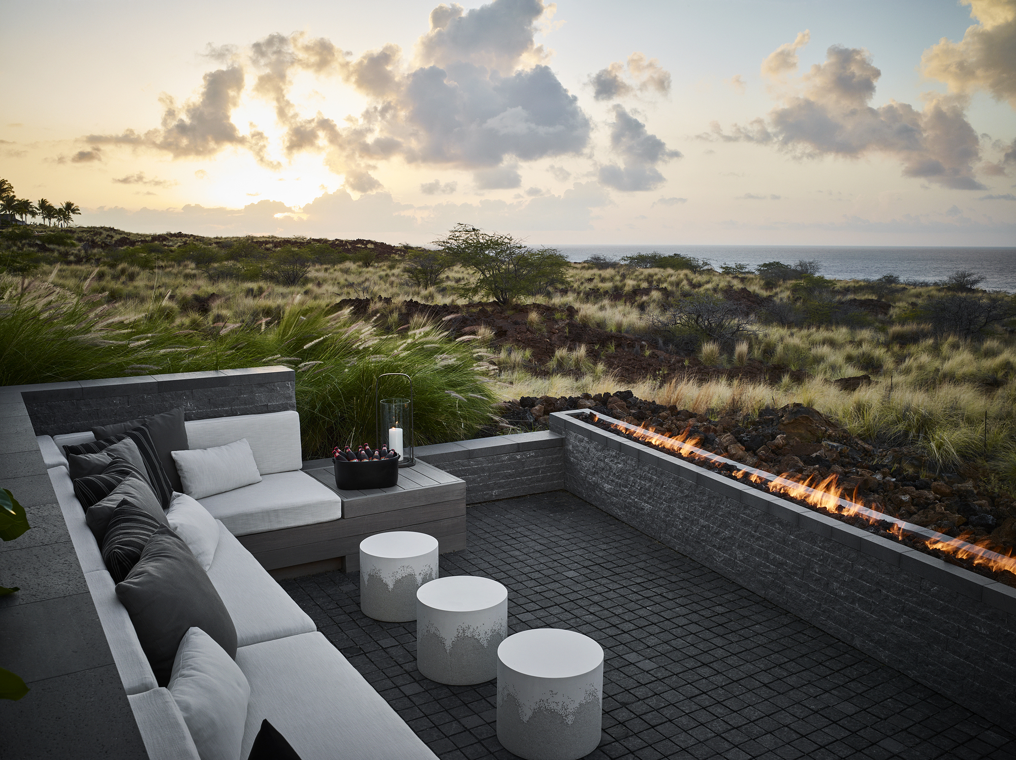 Sunken seating area with linear fire feature and volcanic stone walls facing the ocean at sunset