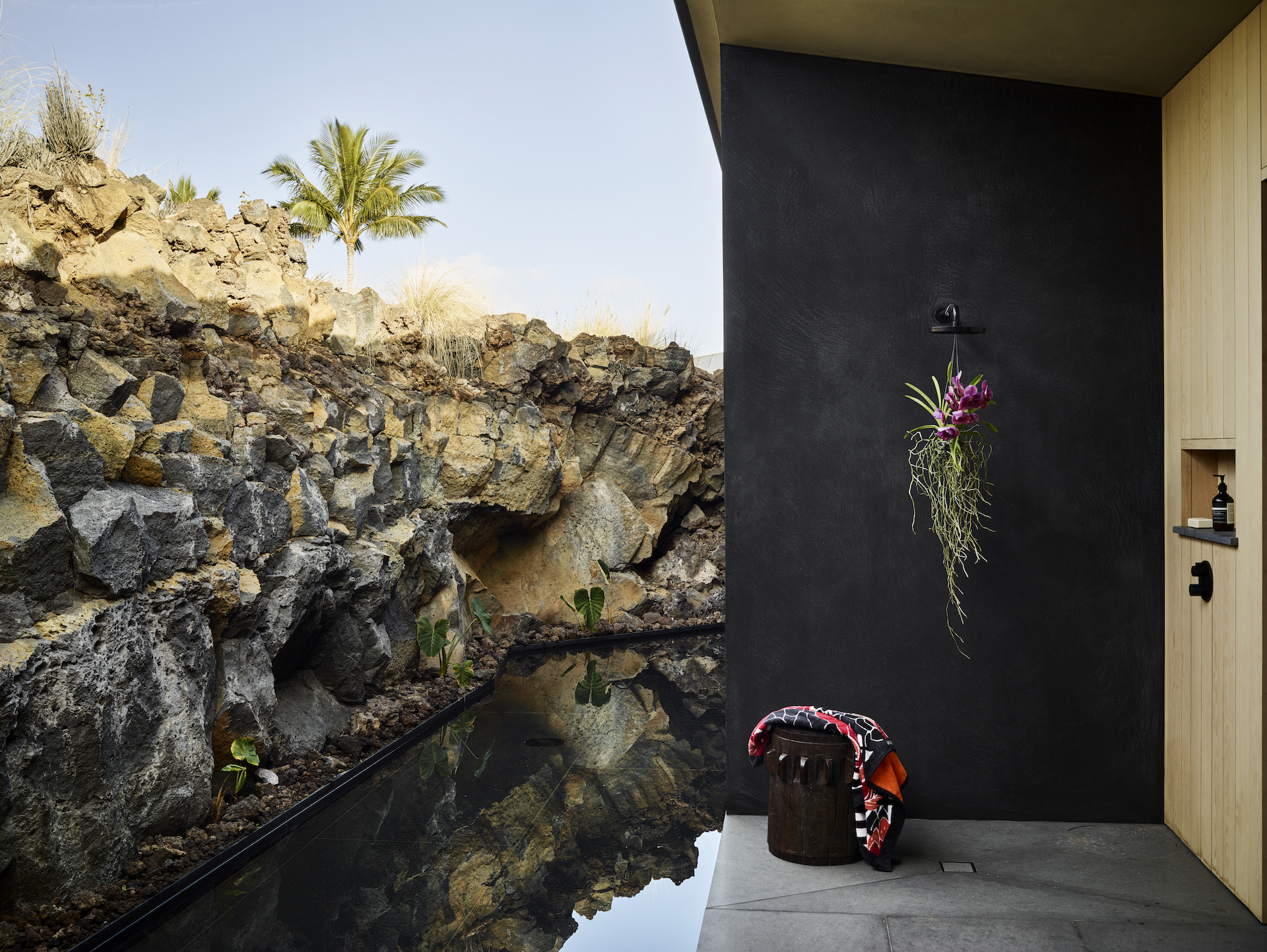 Outdoor shower alcove with black wall against exposed volcanic rock formation