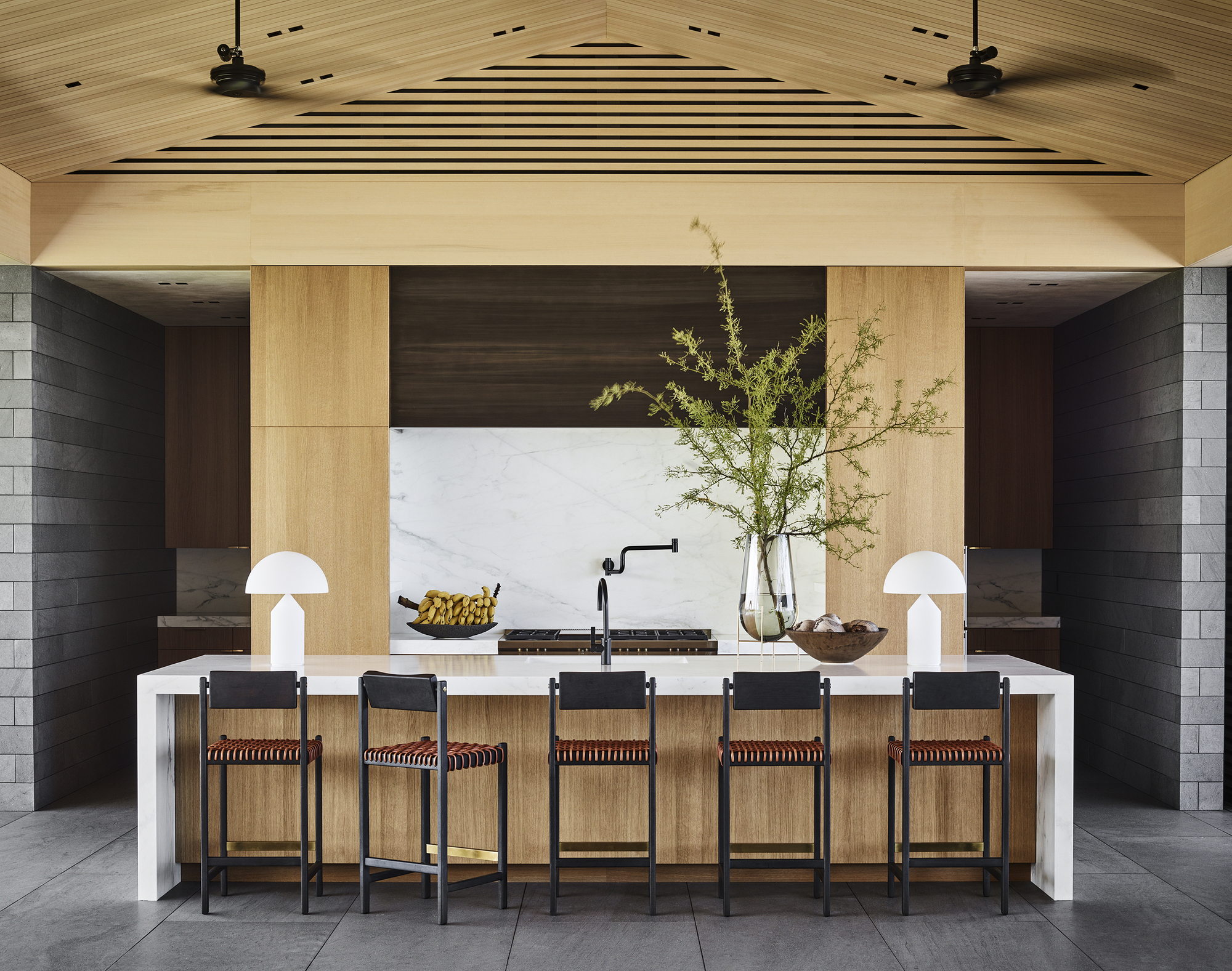Kitchen island with bar seating beneath vaulted timber ceiling and marble backsplash