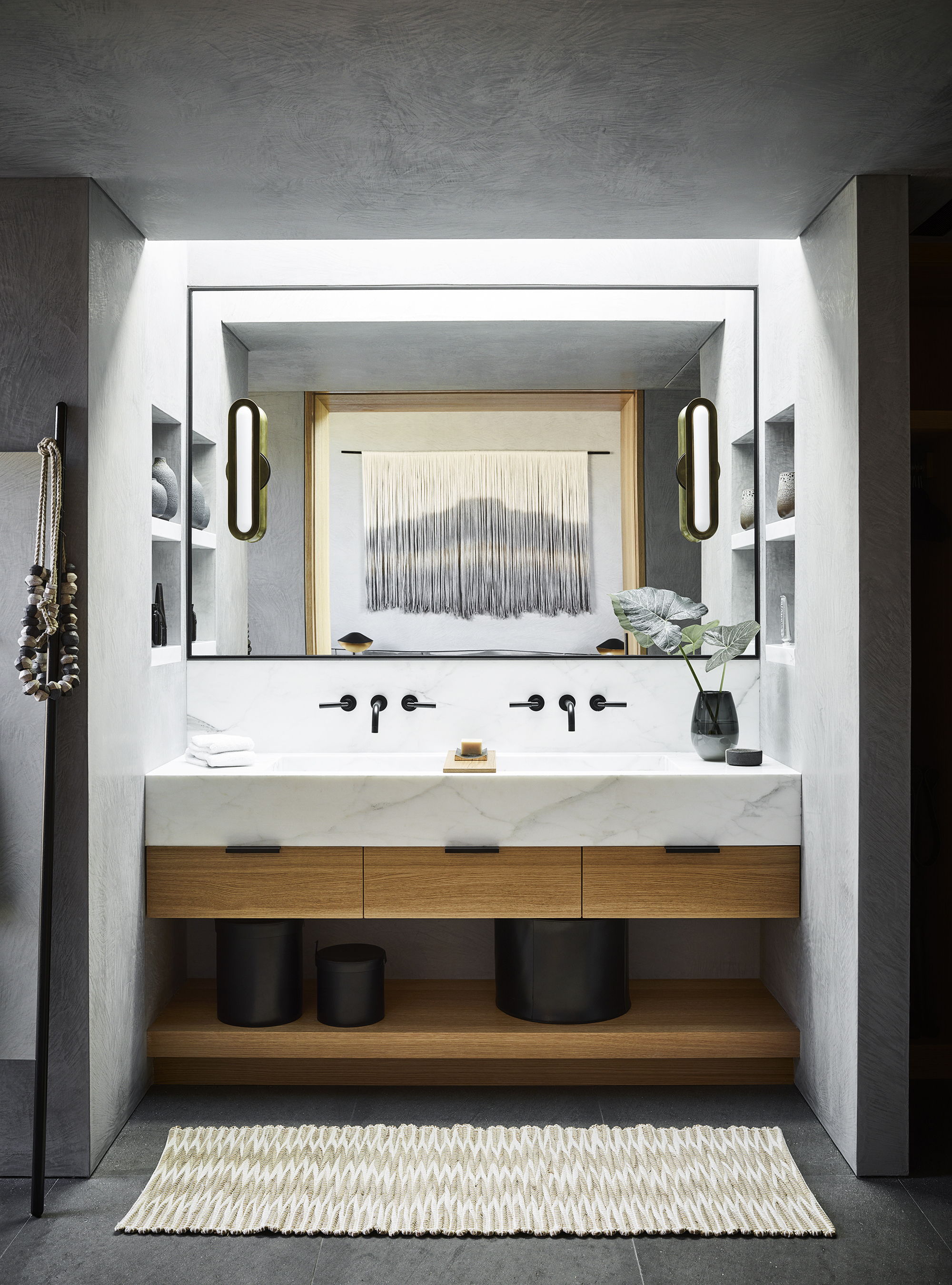 Bathroom vanity with floating stone counter, timber drawers, and oval sconces flanking recessed mirror