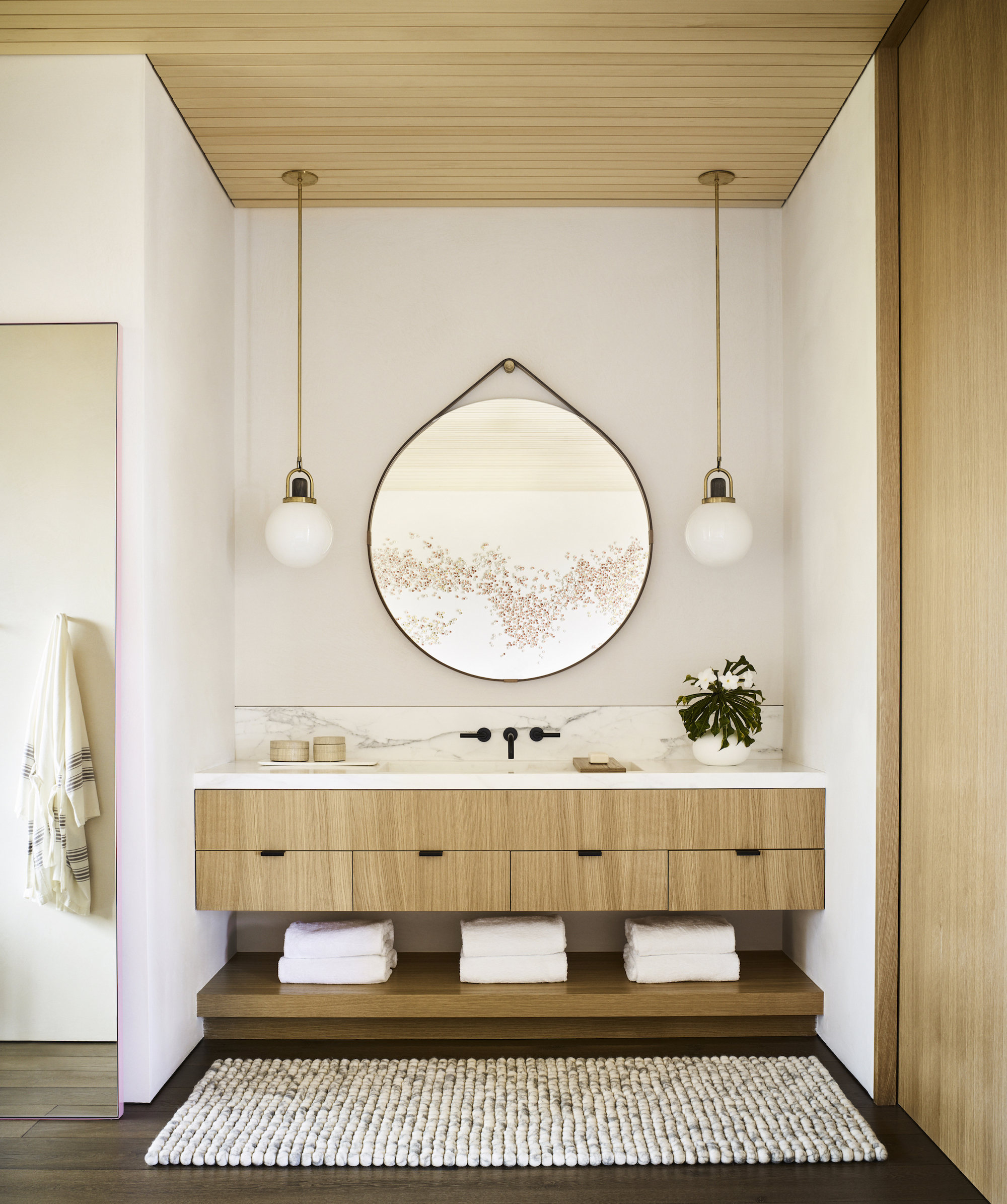 Powder room vanity with timber drawer fronts, circular hanging mirror, and paired pendant lights