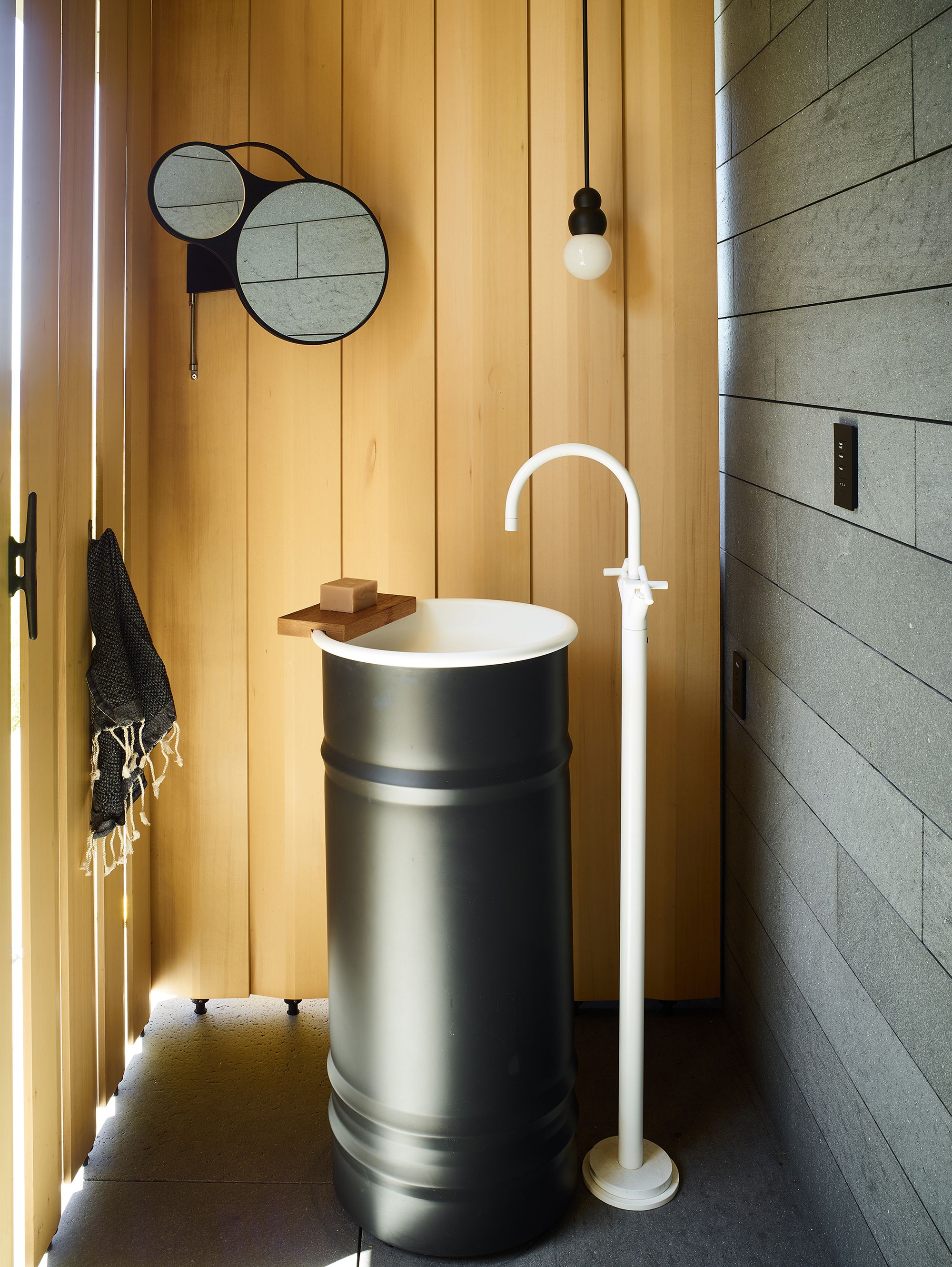 Powder room with cylindrical pedestal sink, vertical timber paneling, and overlapping circular mirrors