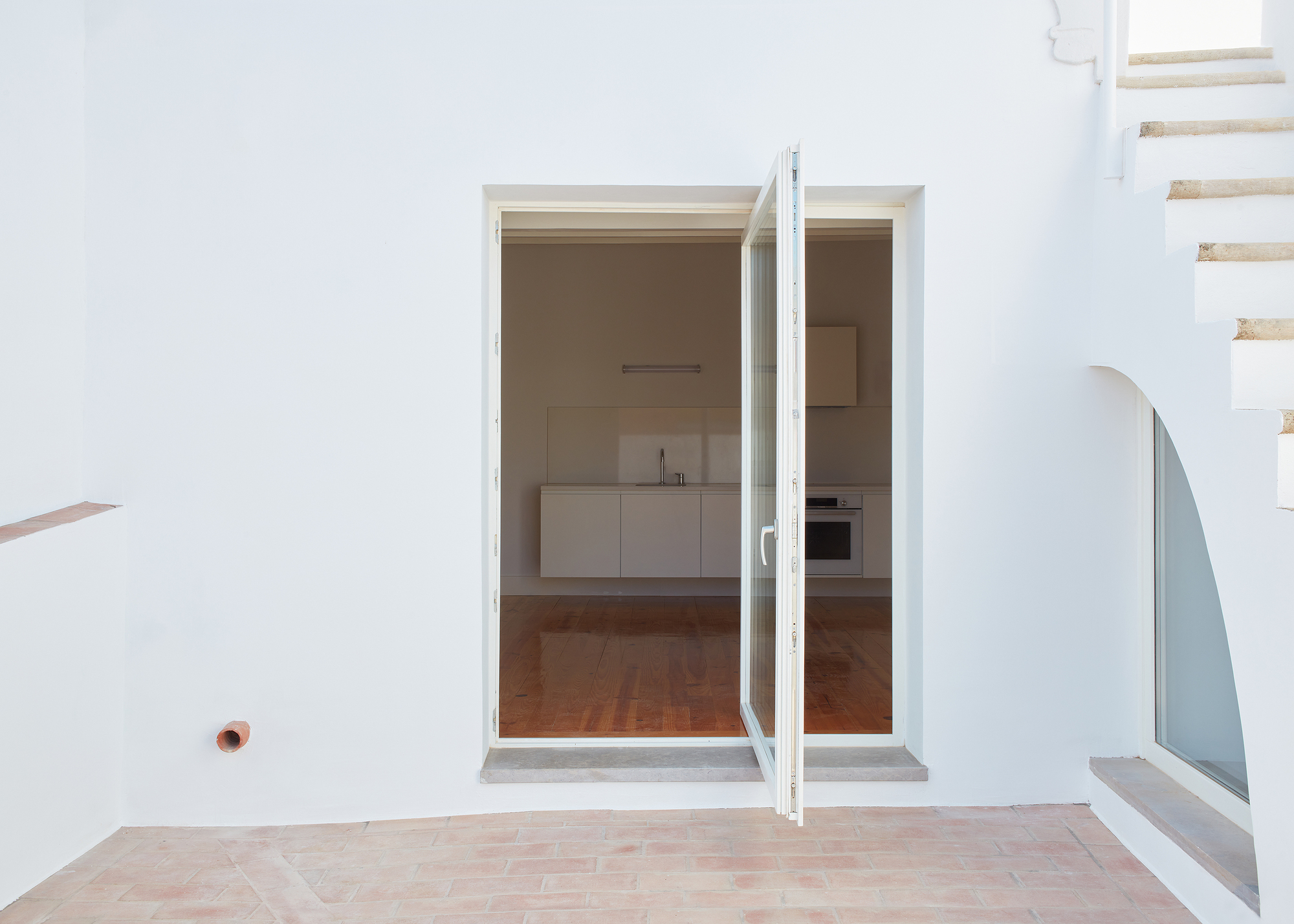 Open glazed door framing a view into the kitchen with terracotta tile flooring