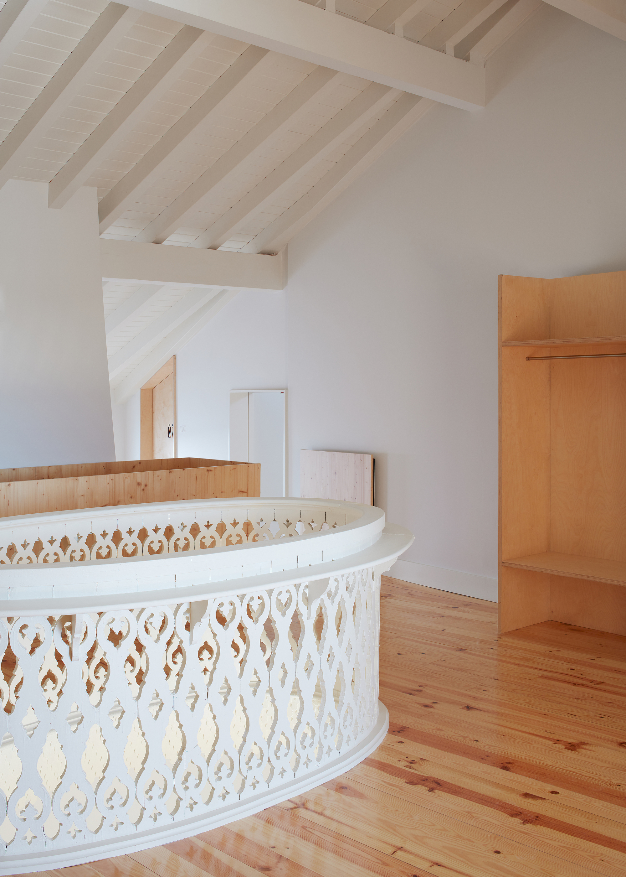 Curved white balustrade with decorative cutouts beside timber joinery under rafters