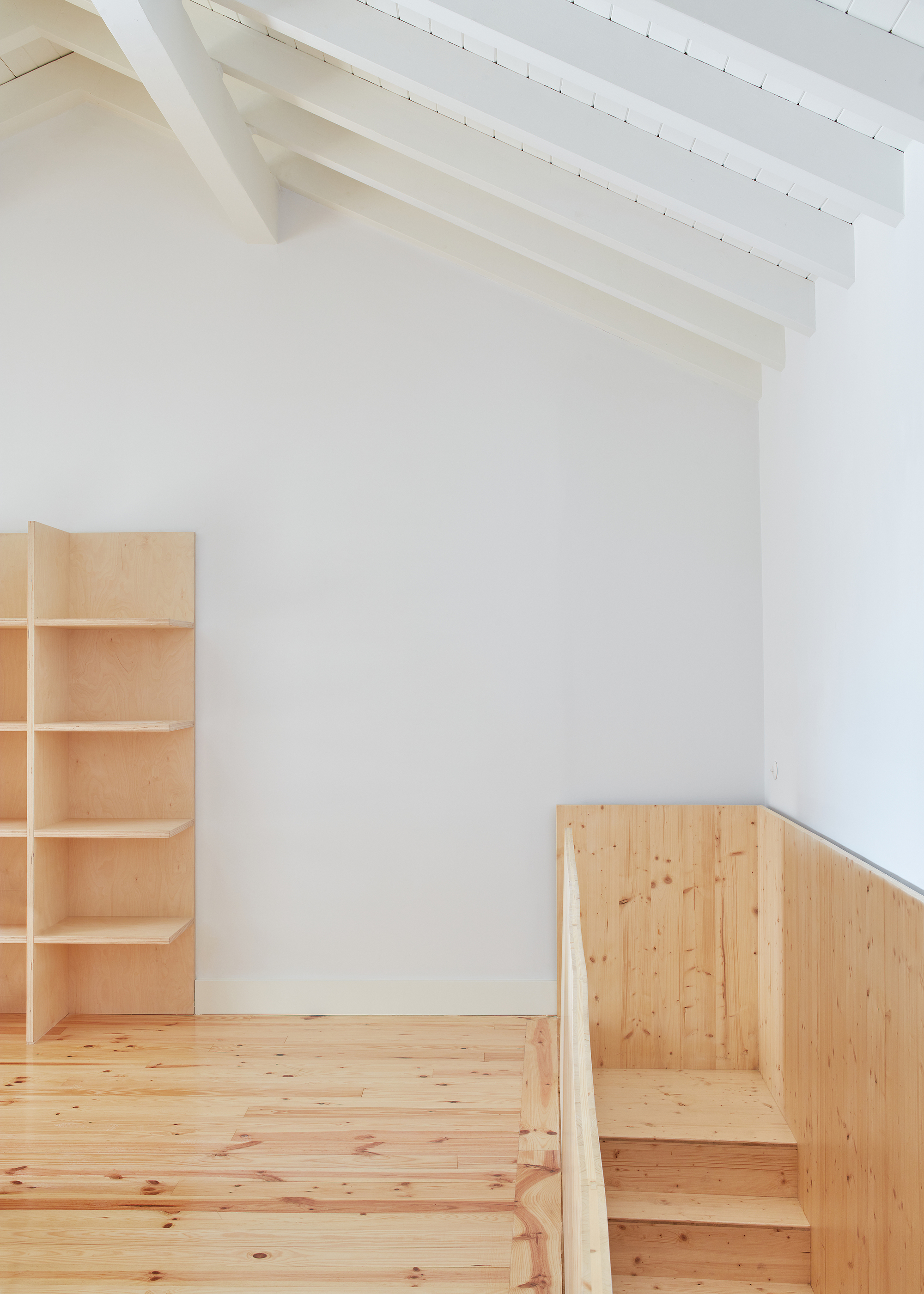 Timber shelving unit and built-in seating beside a stair under painted rafters