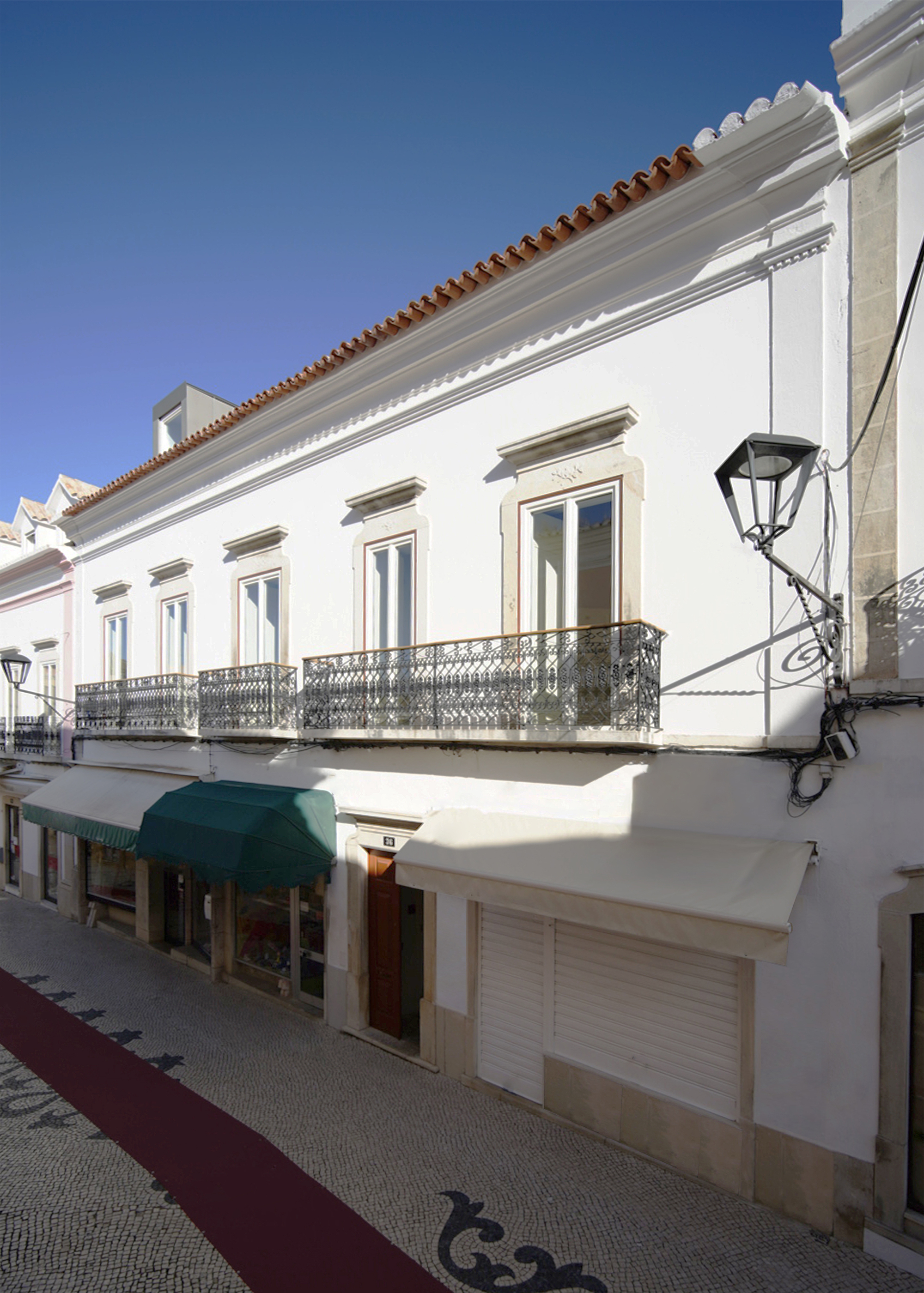 Street view of white stucco facade with wrought iron balcony and terracotta tile roof under clear blue sky