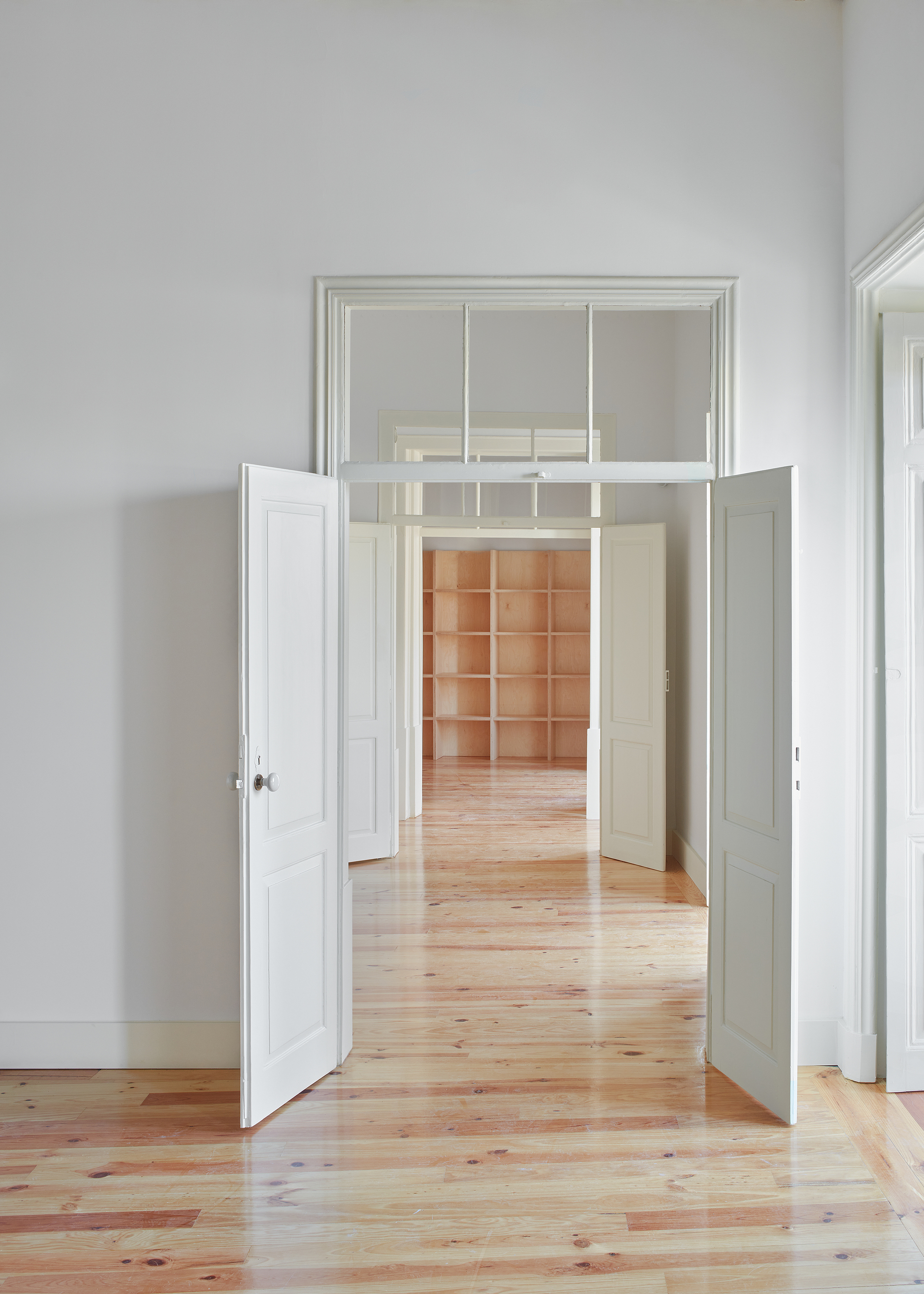 Enfilade of rooms with double doors open showing pine floorboards and transom windows in soft light