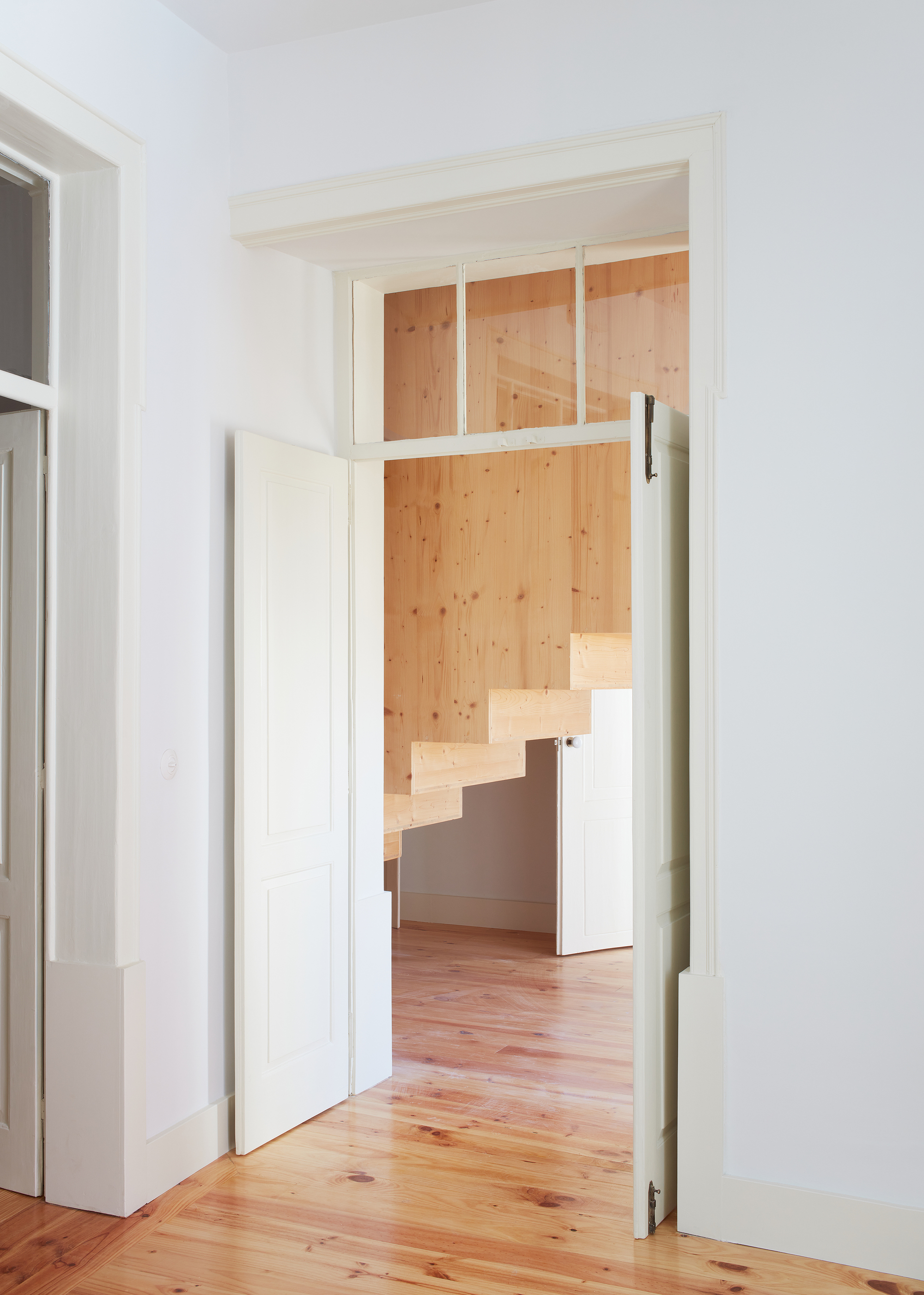 Doorway framing view into timber lined room with cantilevered stair through horizontal transom glazing