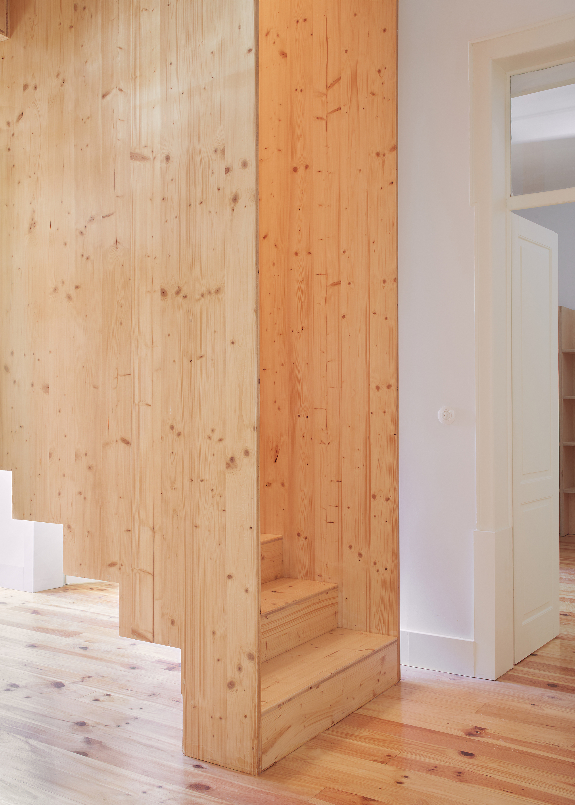 Light wood plank column with integrated bench seating beside white walls and doorway