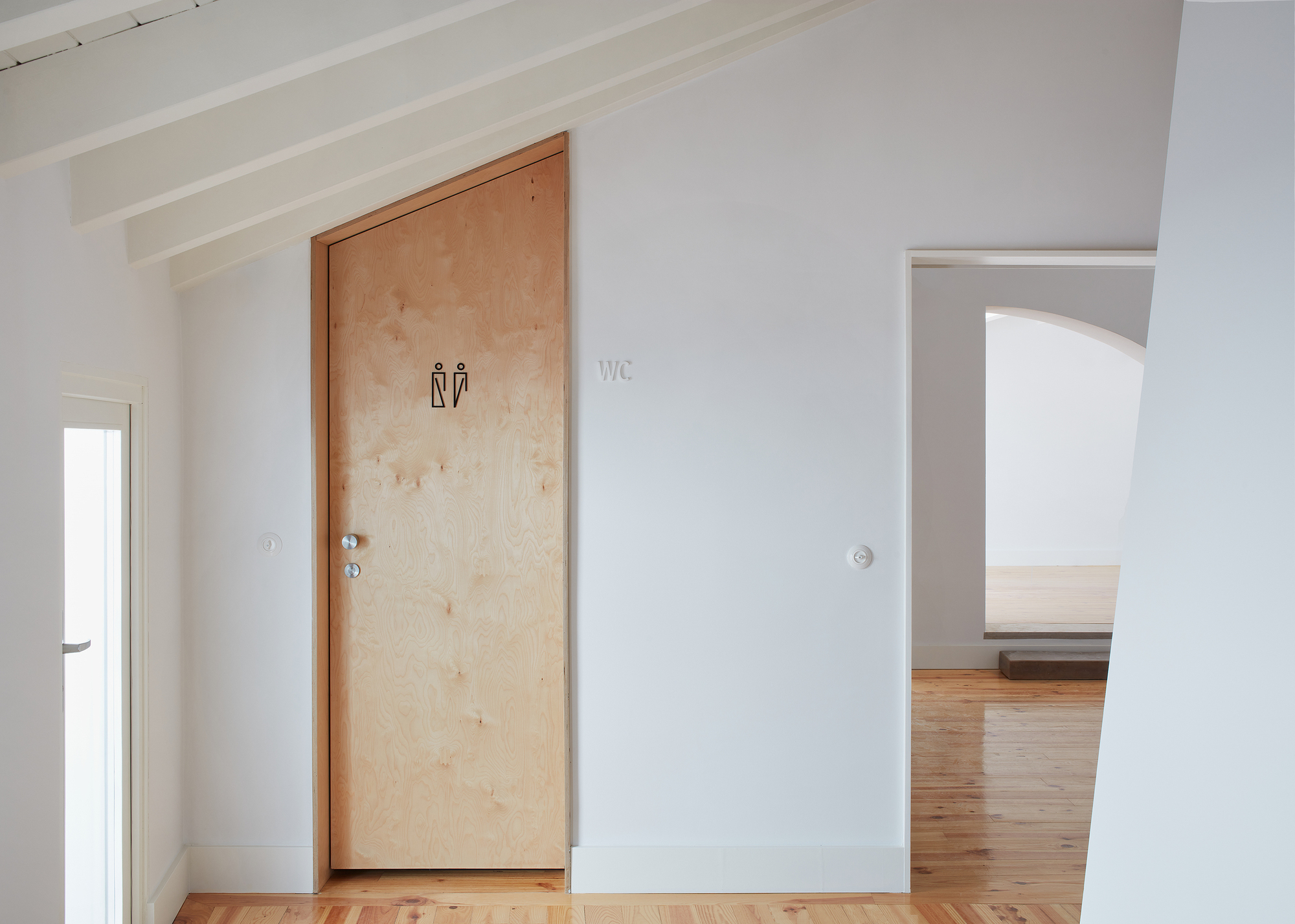 Plywood restroom door with pictogram signage set in white painted walls with exposed ceiling beams