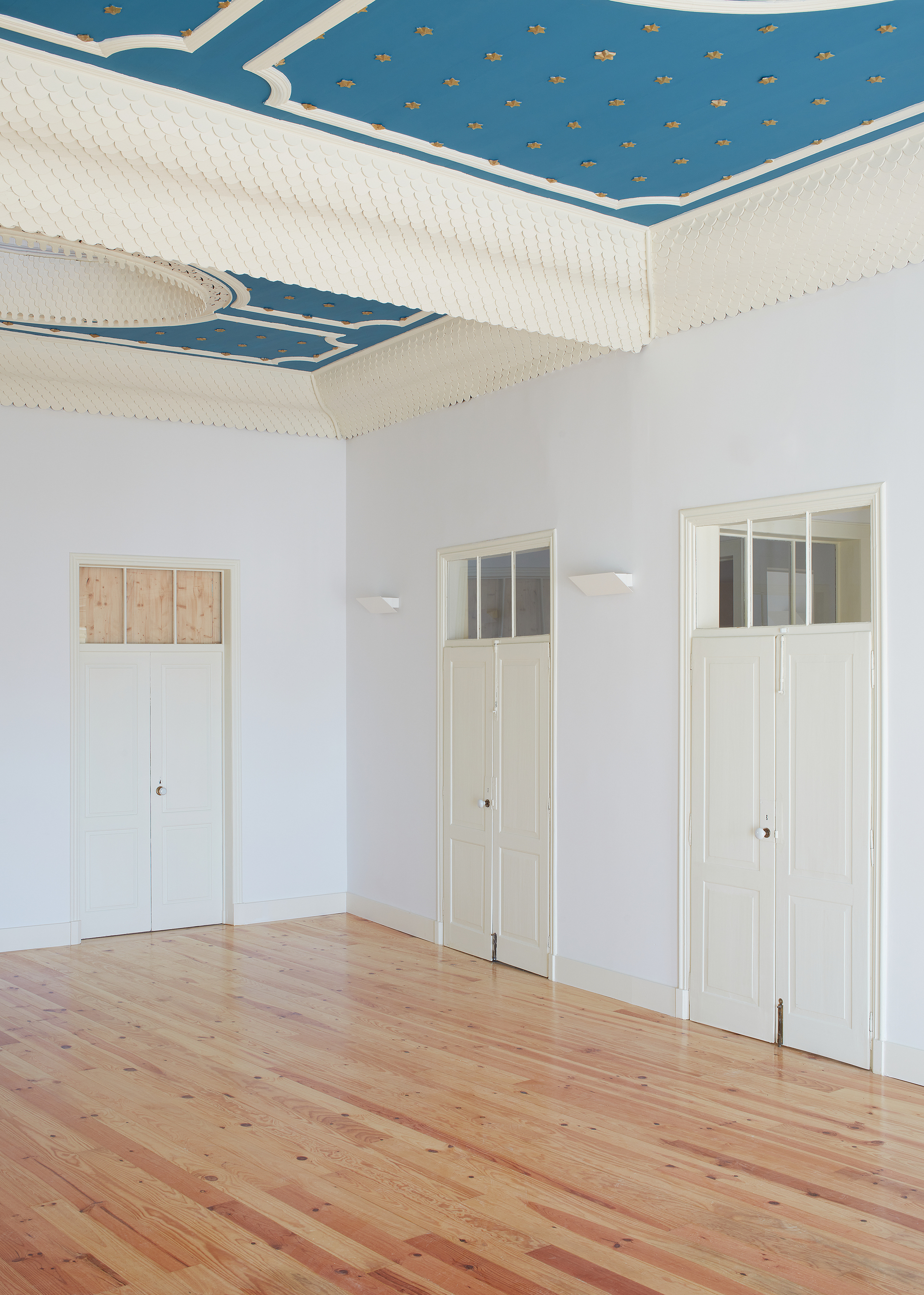 Three tall doors with transom windows beneath restored blue and gold painted ceiling with star pattern