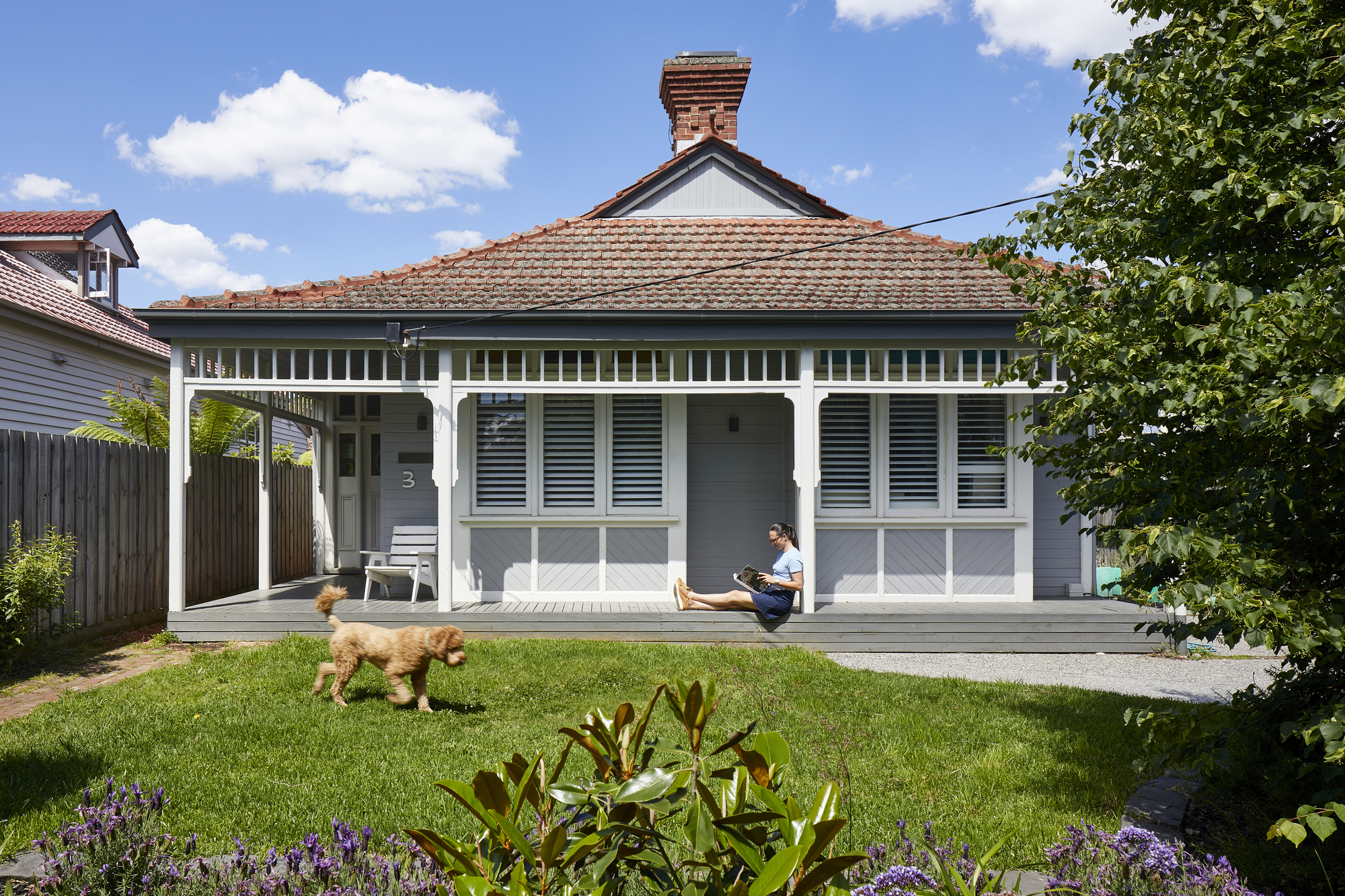 Front elevation of the existing weatherboard cottage with terracotta tile roof, decorative trim and person seated on deck