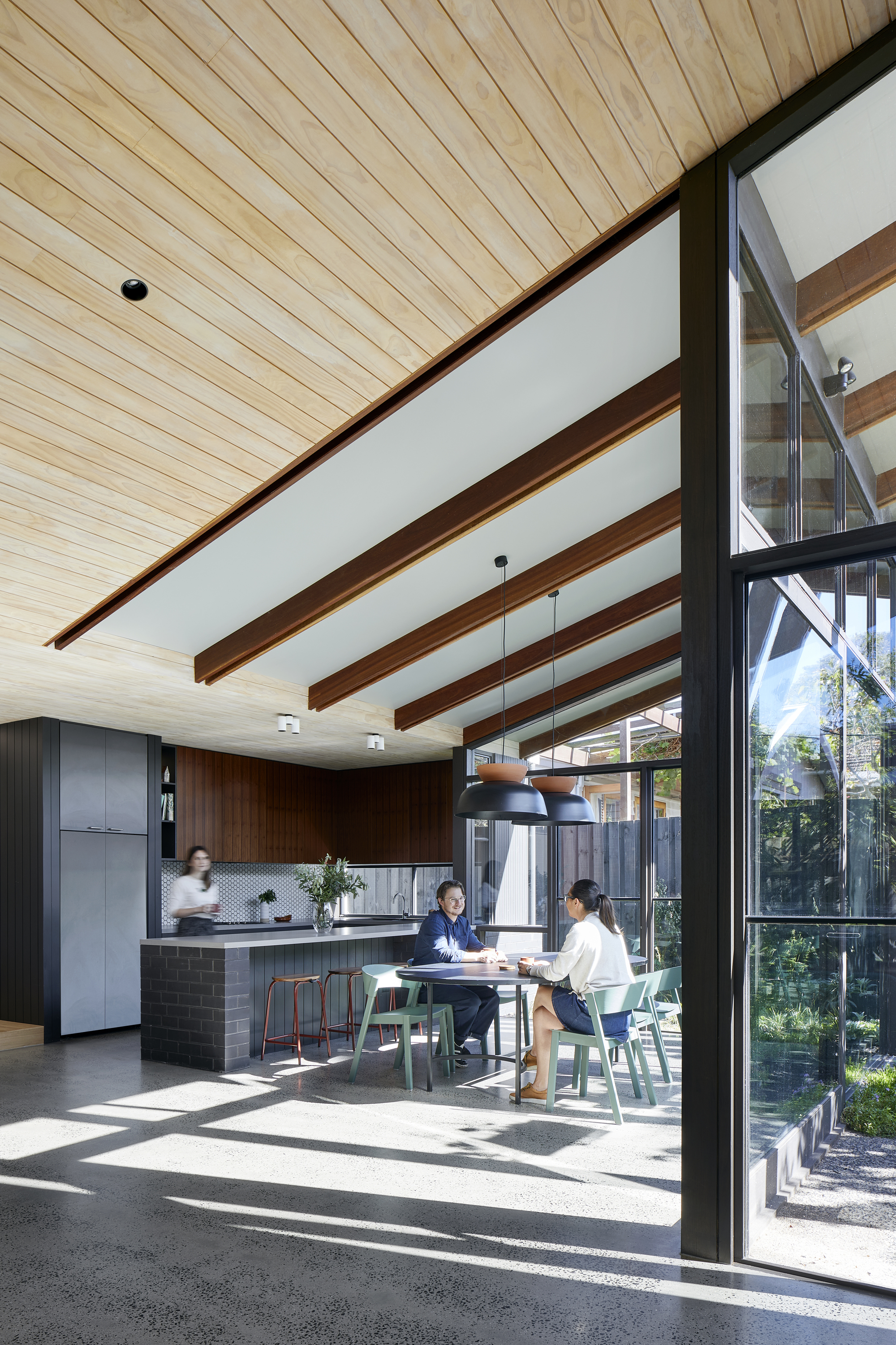 Open-plan kitchen and dining area with exposed timber beams and two people seated at a table