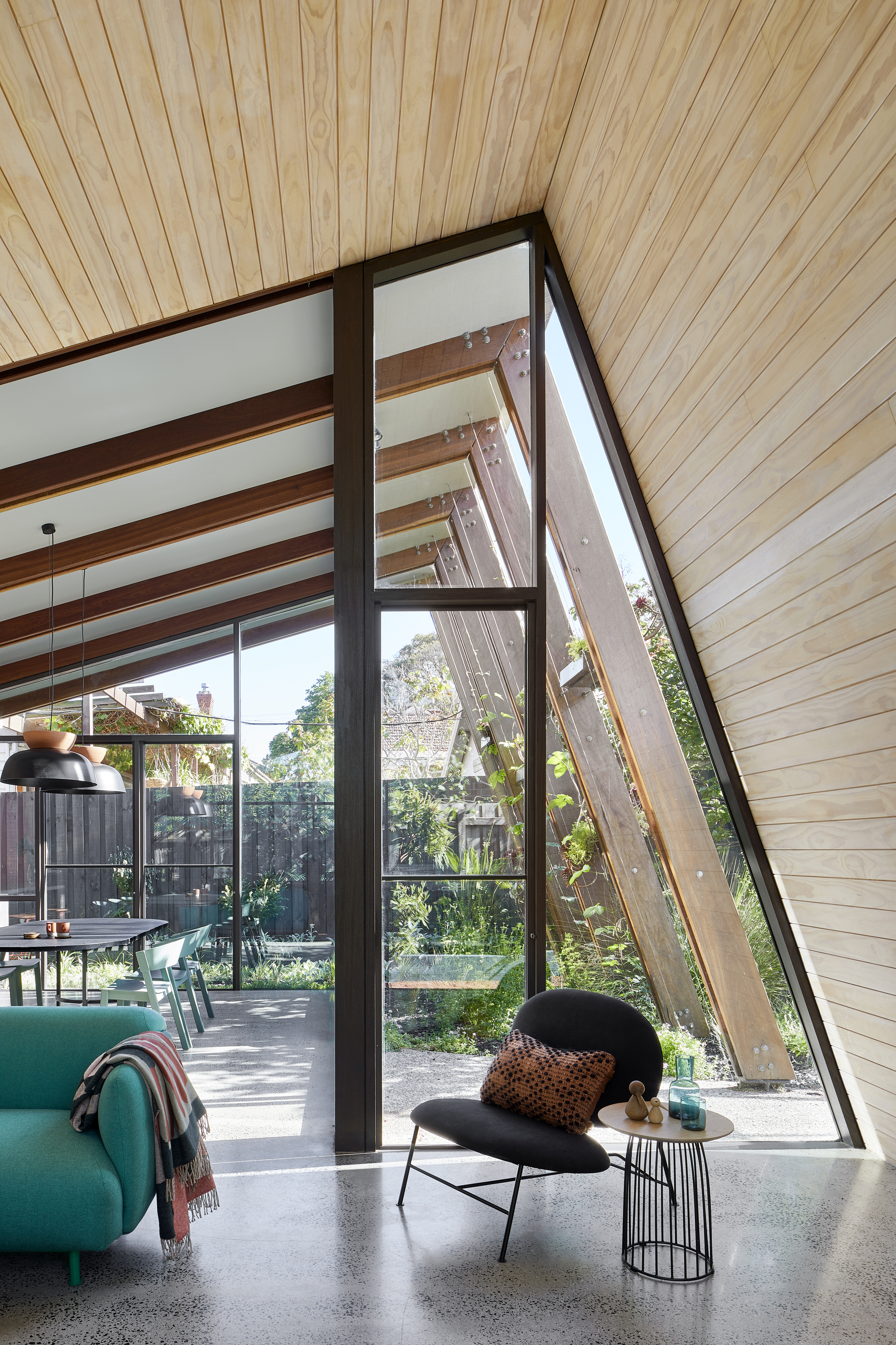 Slanted timber-lined ceiling above glazed corner opening with exposed steel frame and polished concrete floor