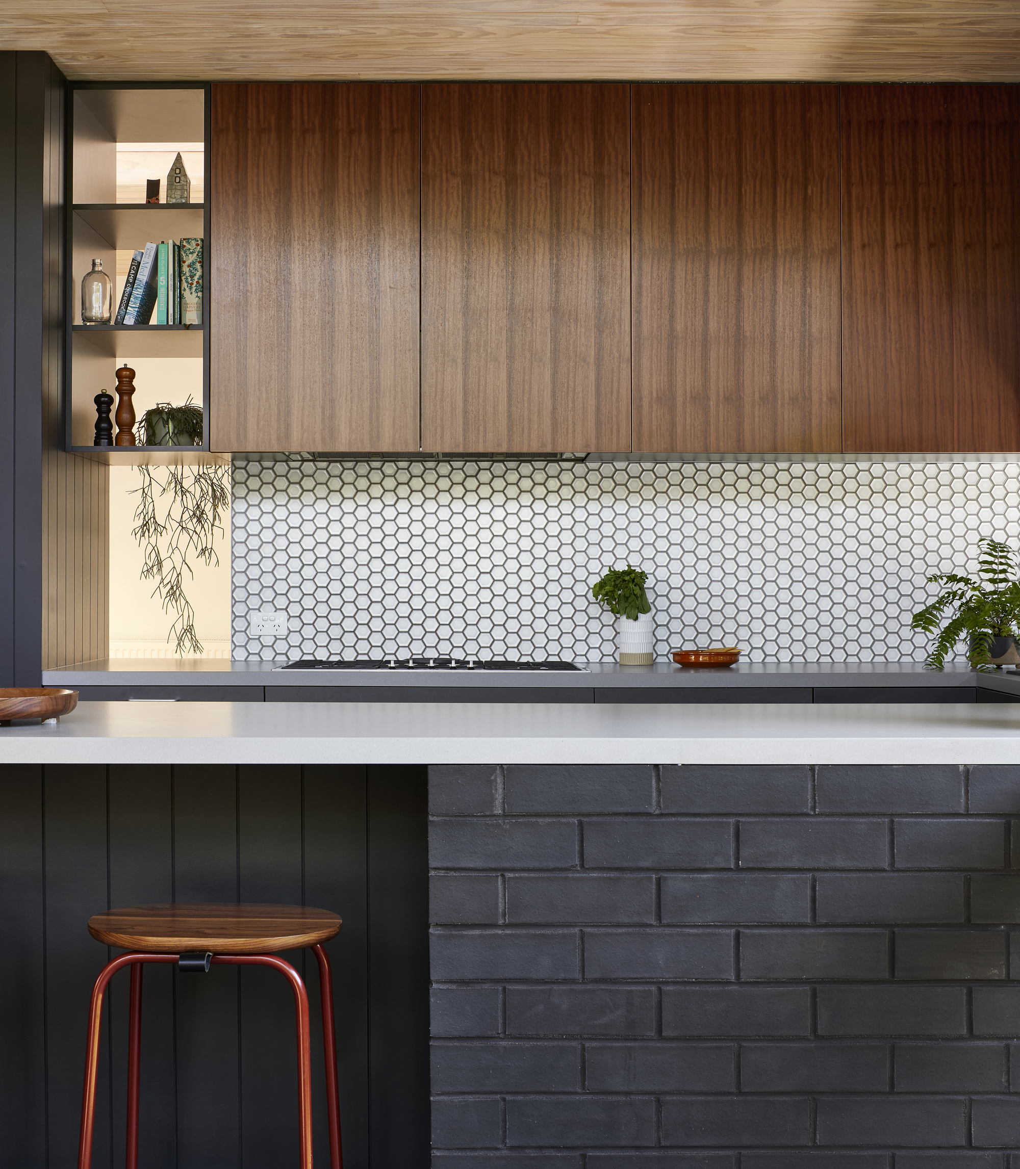 Kitchen counter with white hexagonal mosaic tile backsplash beneath timber cabinetry and open shelving
