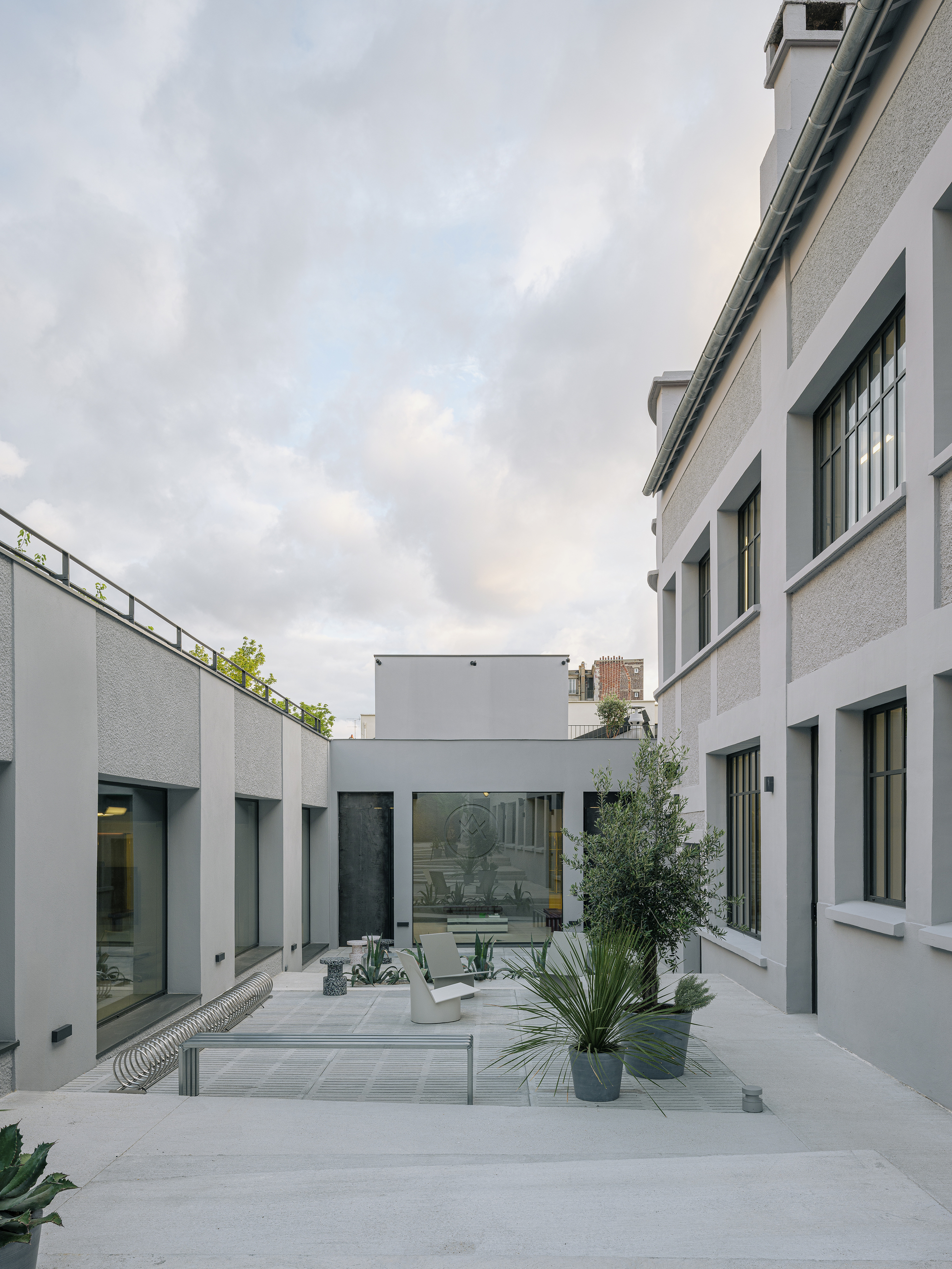 Courtyard with light grey pavers and planted beds between white rendered walls under cloudy dusk sky