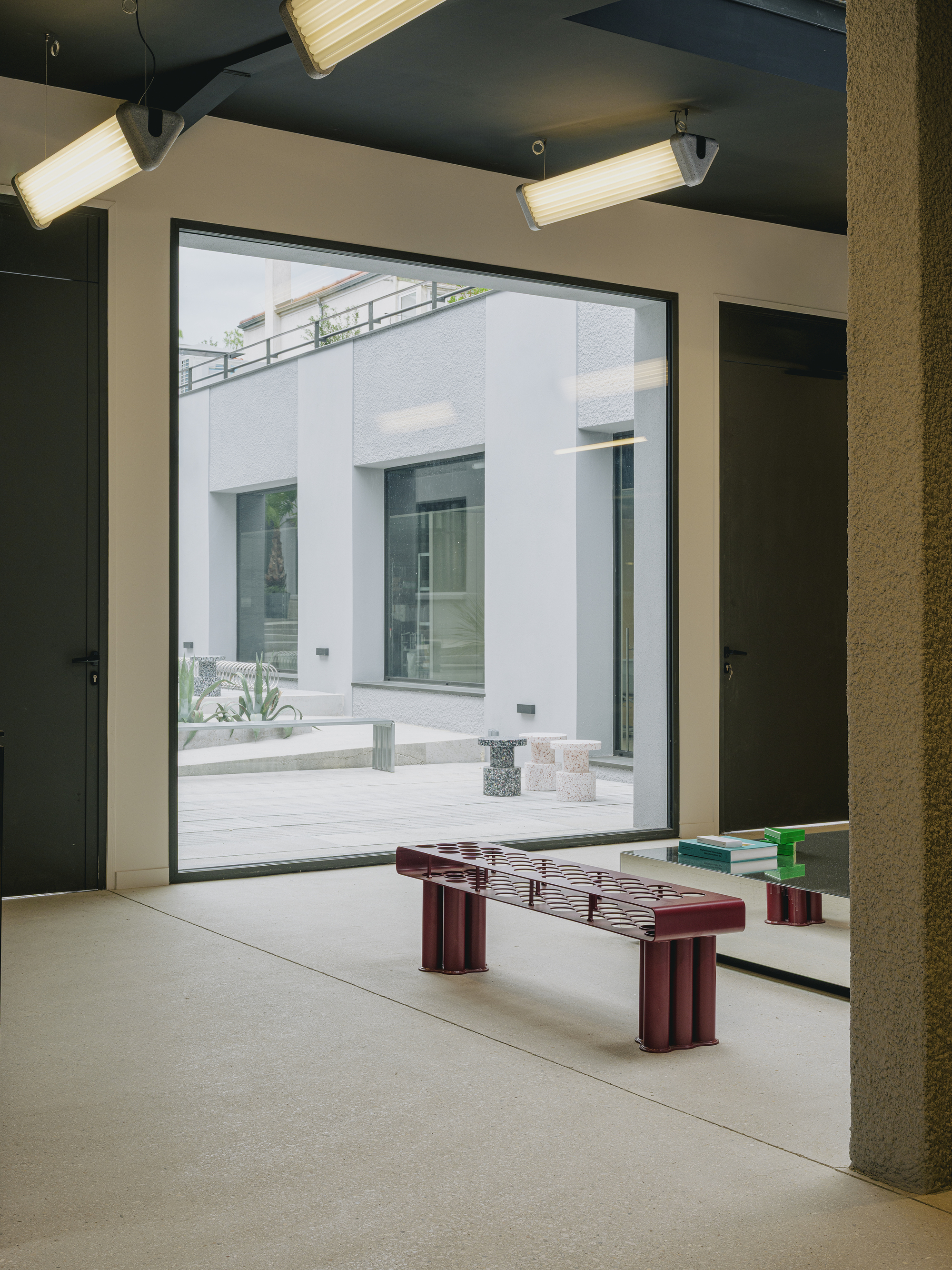 Interior room framing courtyard through full-height glazing with maroon slatted bench in foreground