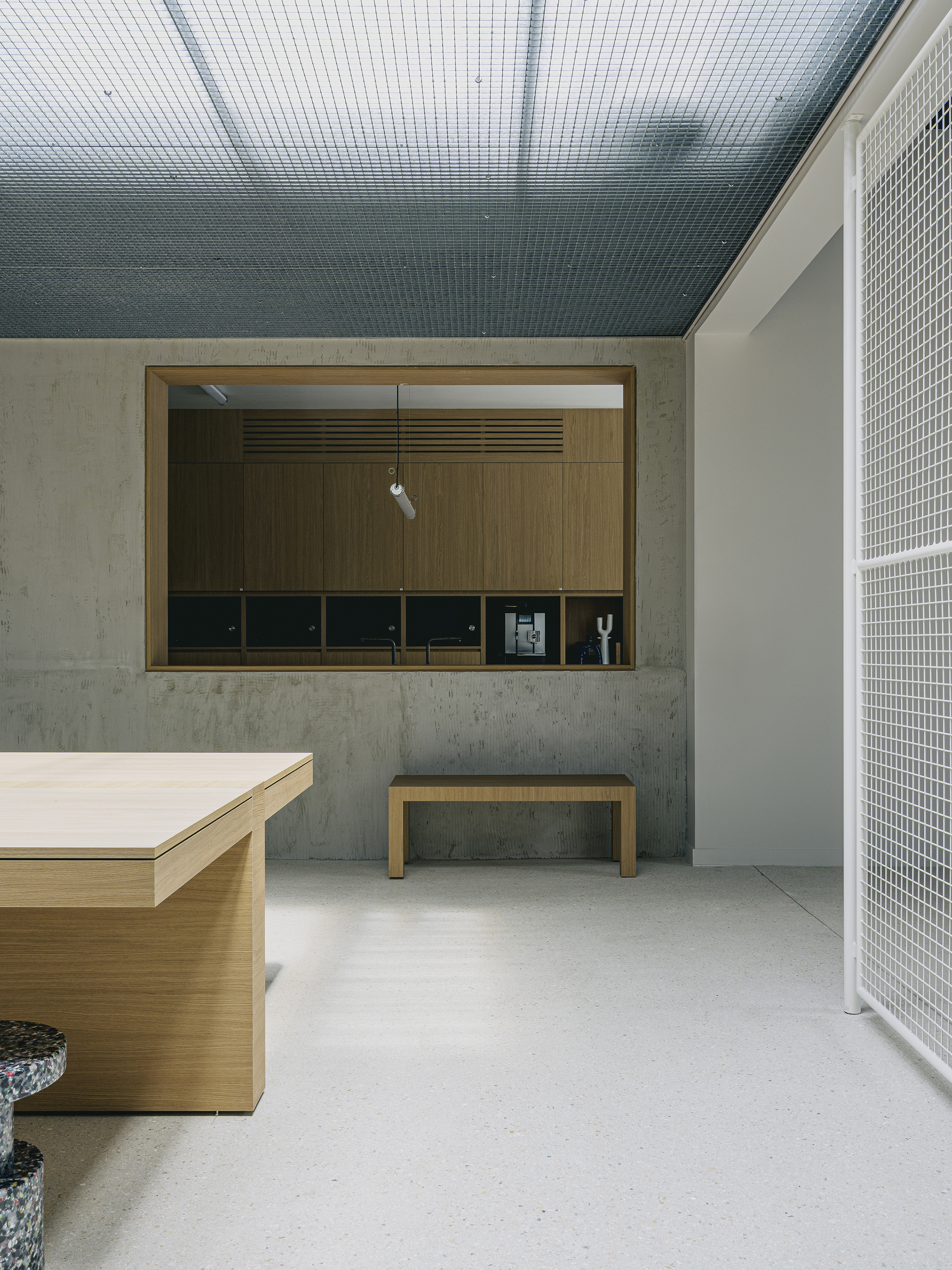 Interior space with mesh ceiling, concrete walls, timber-lined service window, and white mesh partition