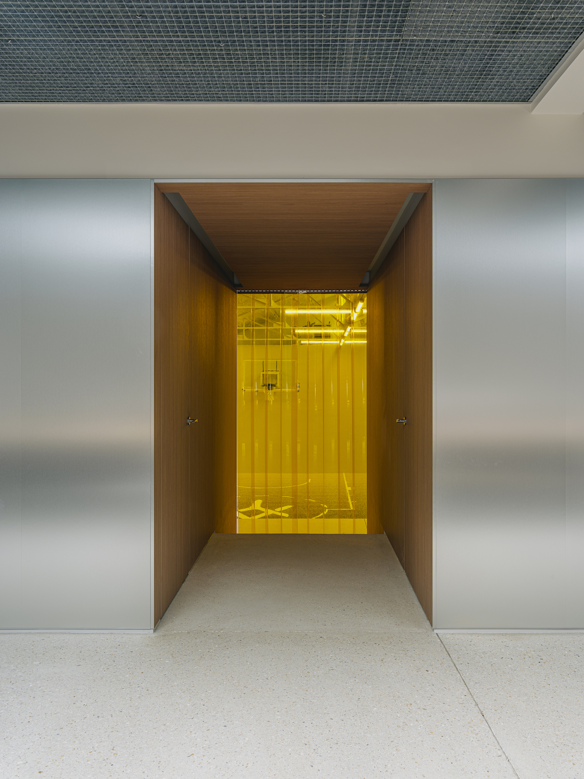 Wood-lined corridor leading to a yellow-lit elevator vestibule framed by brushed metal walls