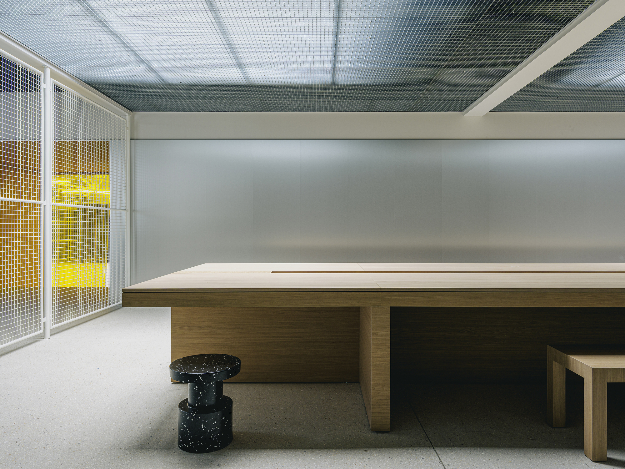 Timber conference table with terrazzo cylinder stools beneath a translucent gridded ceiling