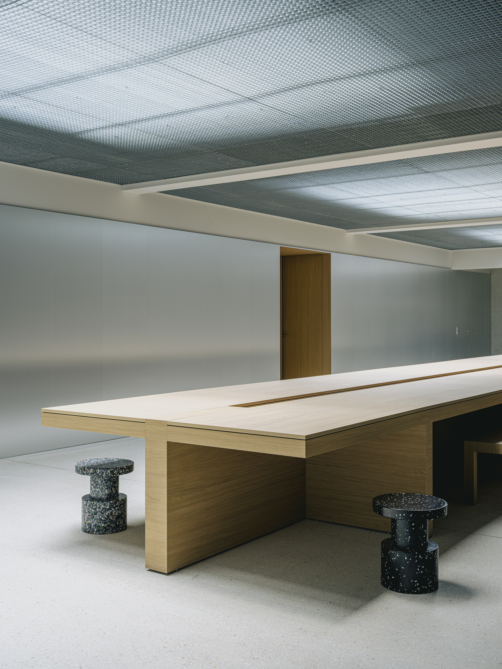 Close-up of the timber table edge with speckled terrazzo stools under recessed ceiling panels