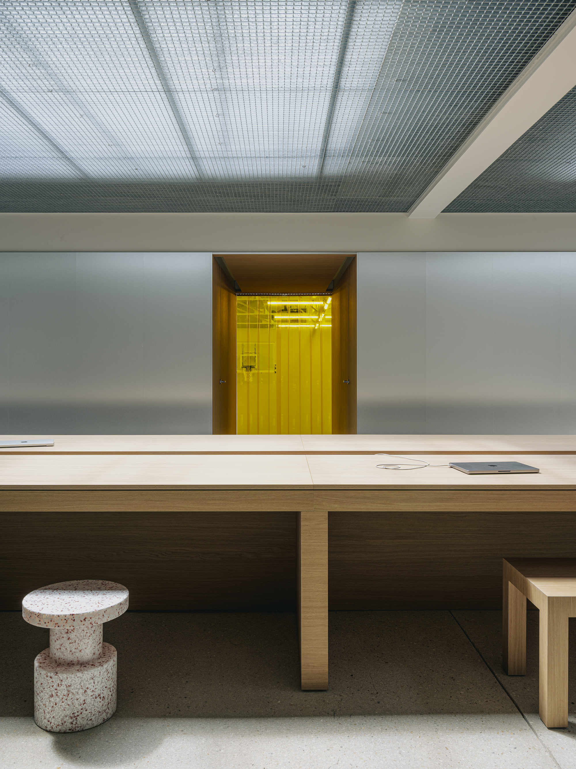 View across the table surface toward yellow-lit doorway with terrazzo stool in foreground