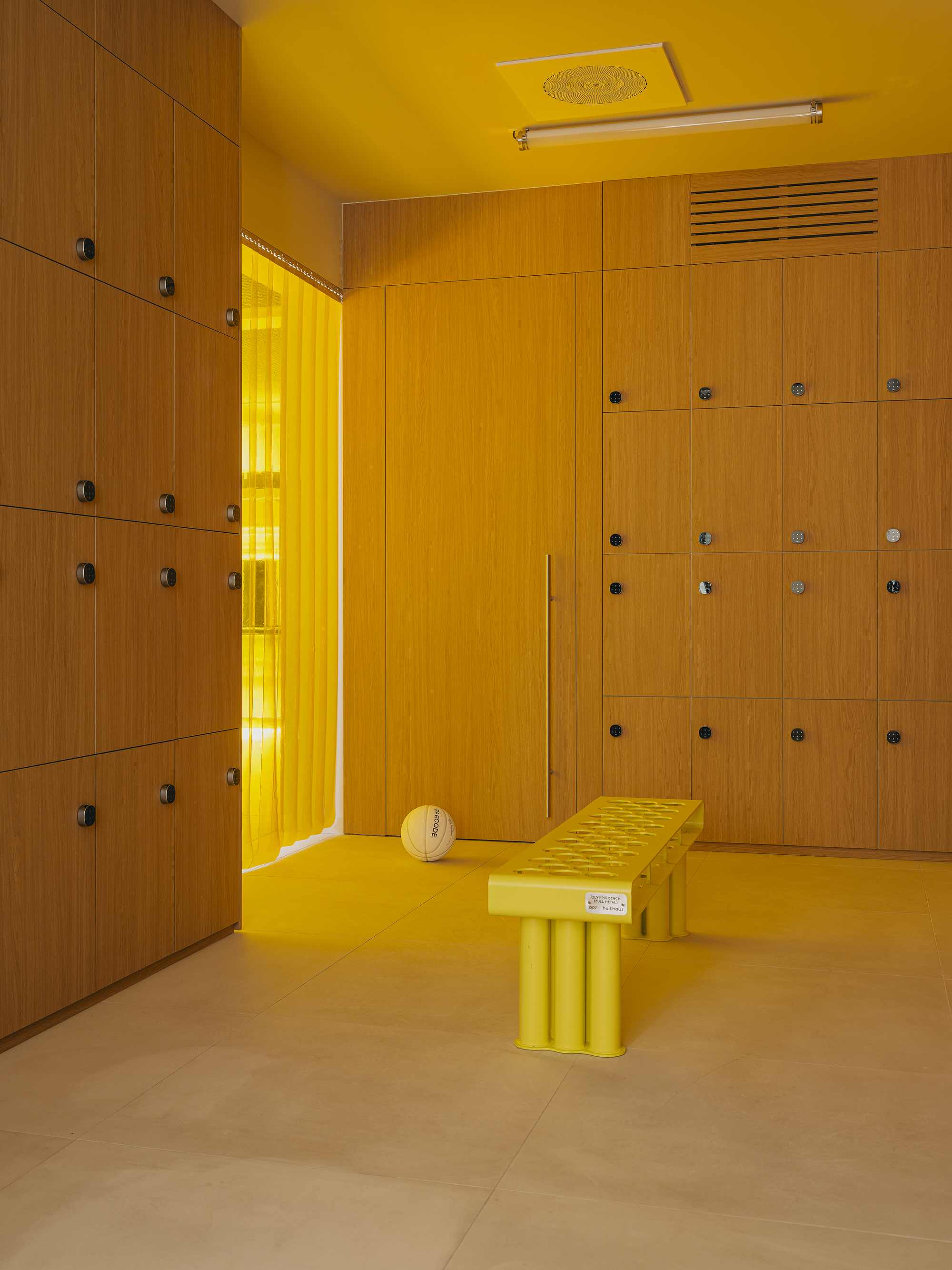 Locker room with yellow walls and ceiling, timber lockers with metal hardware, and yellow bench