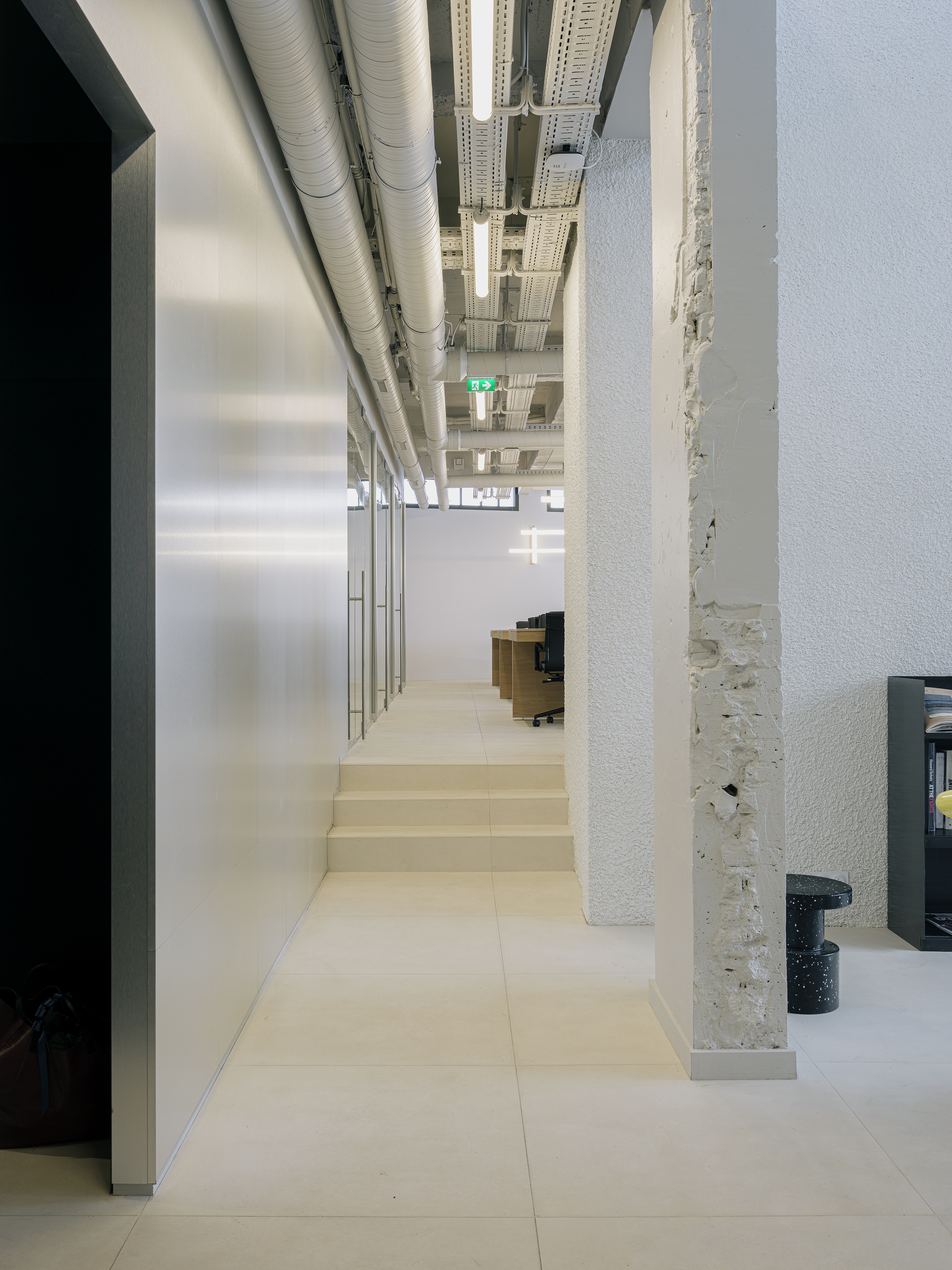 Wide interior steps rising between white concrete column and glazed partition with exposed ductwork above