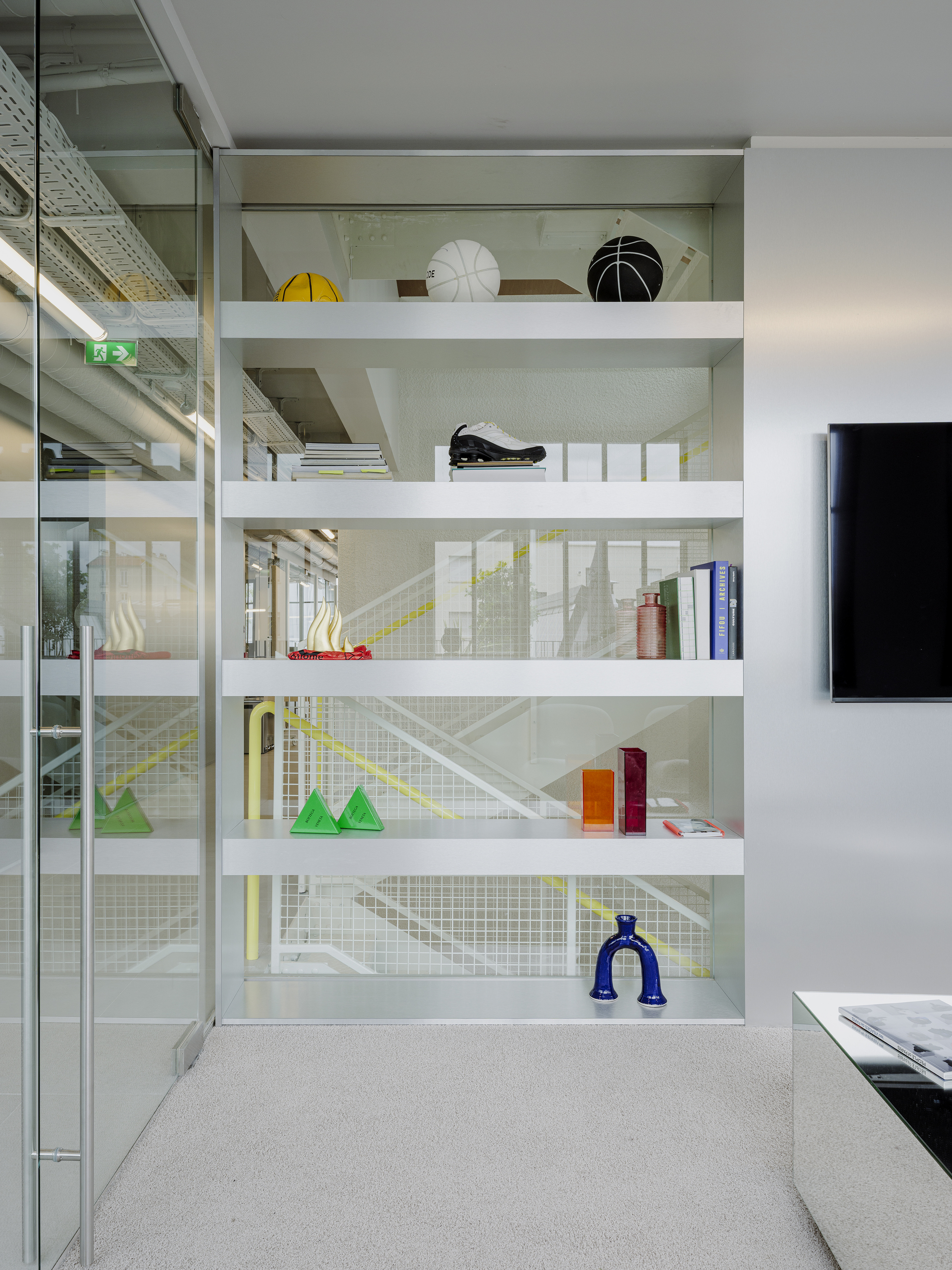 White shelving unit displaying colorful objects behind wire mesh panels with glass partitions beyond