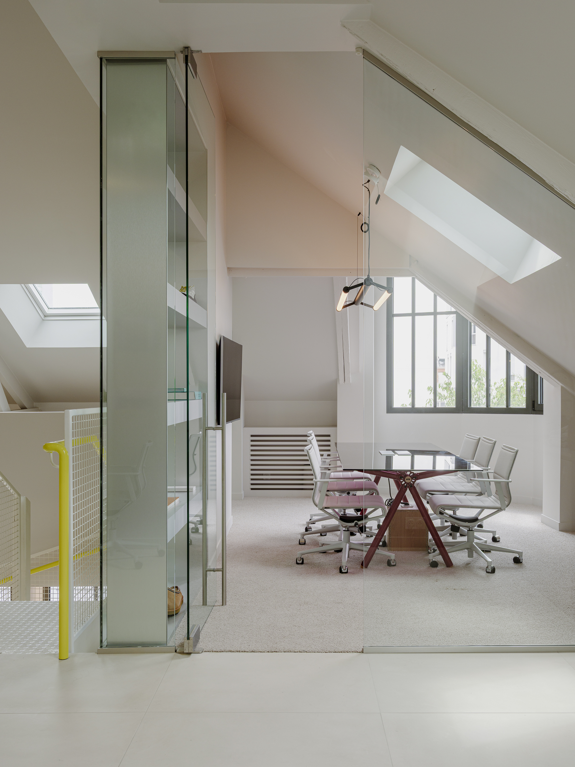 Attic meeting room with sloped ceilings, skylights, and glass partition separating workspace below