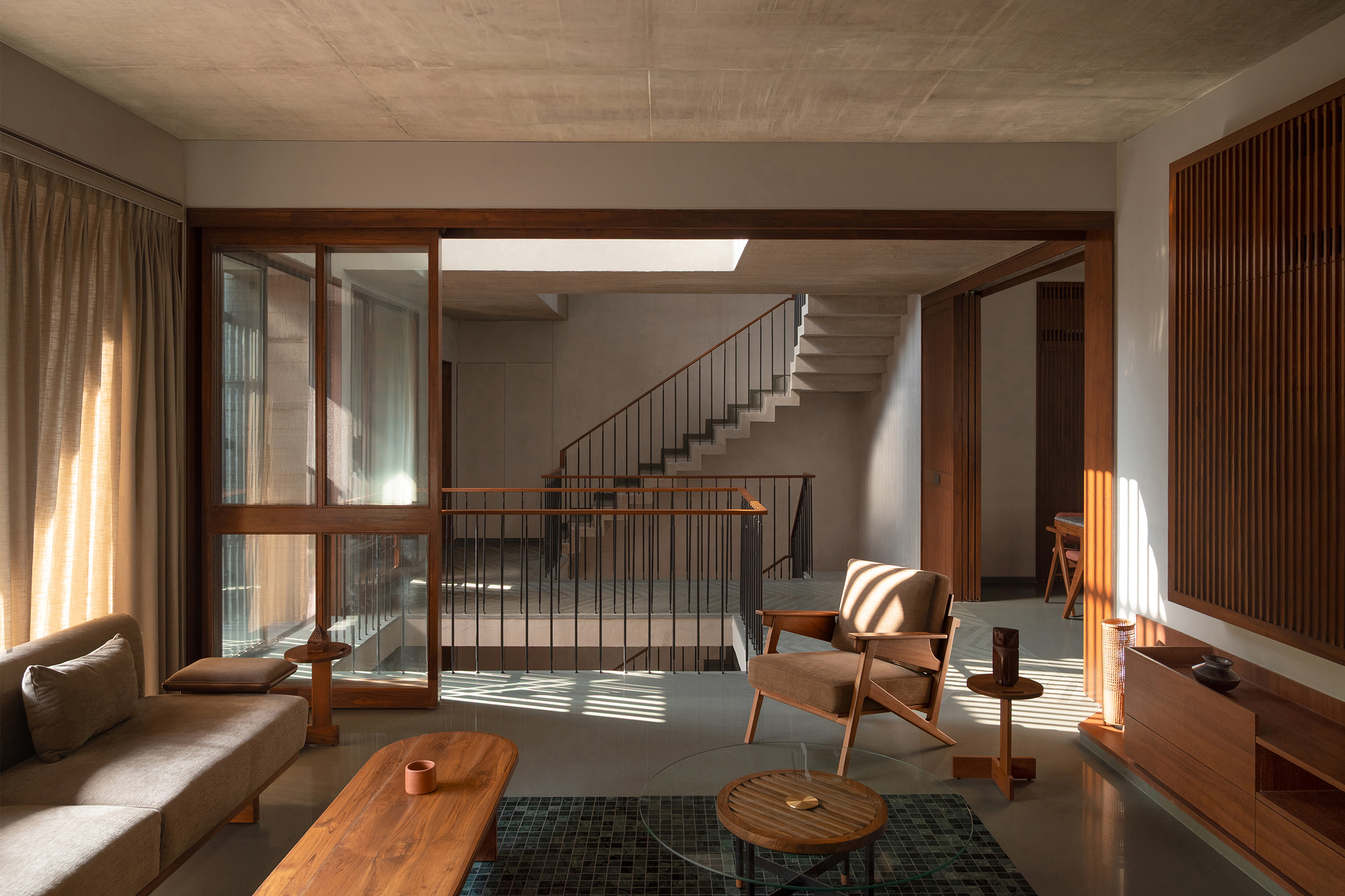 Double-height living room with cantilevered concrete staircase bathed in afternoon sunlight