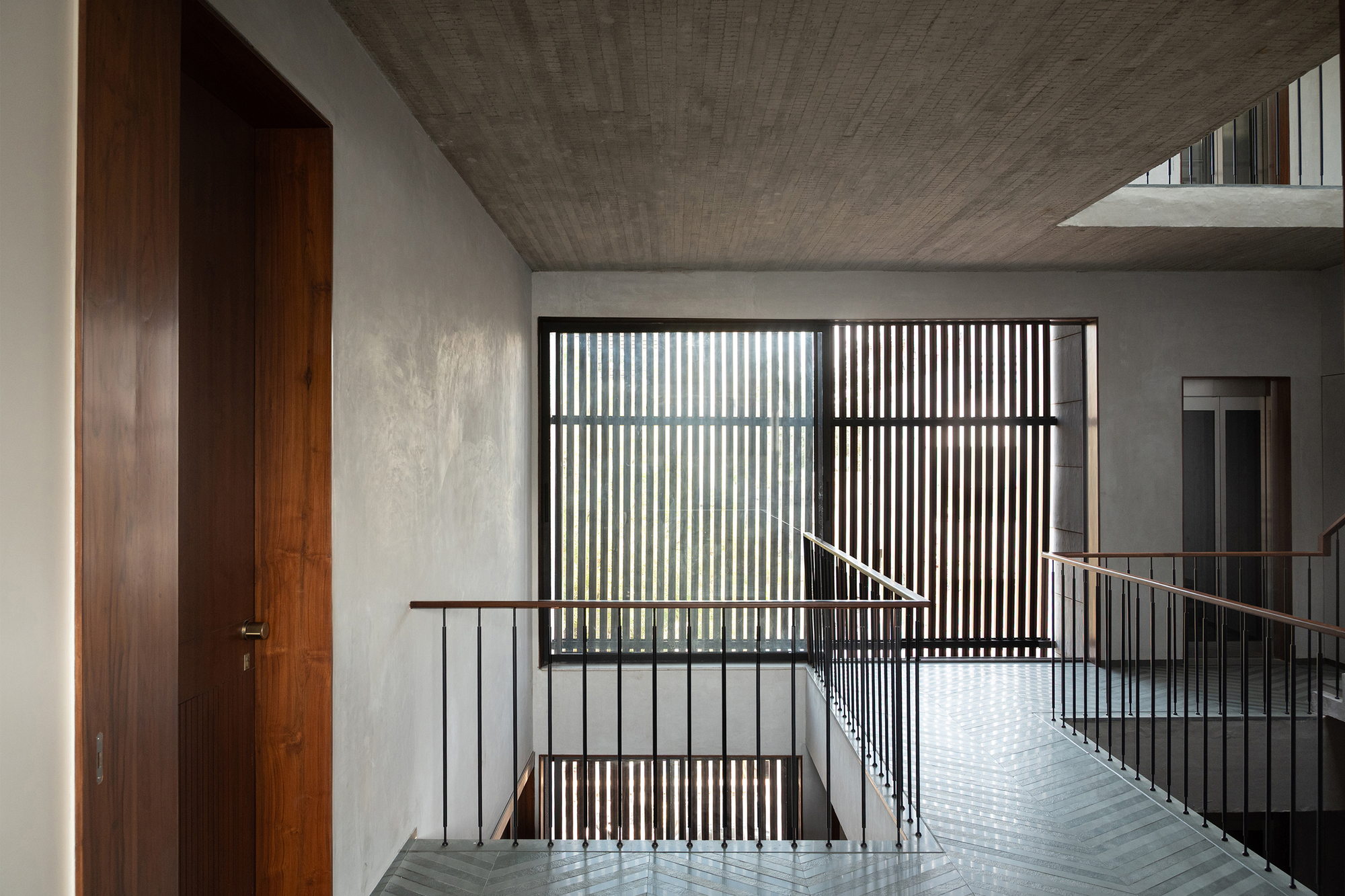 Upper landing with vertical timber slat screen filtering daylight into the stairwell with concrete ceiling