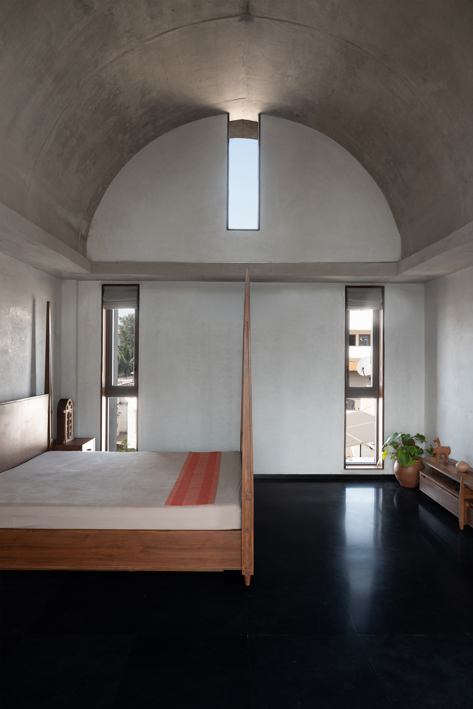 Bedroom beneath a concrete barrel vault with a vertical slot skylight at the apex