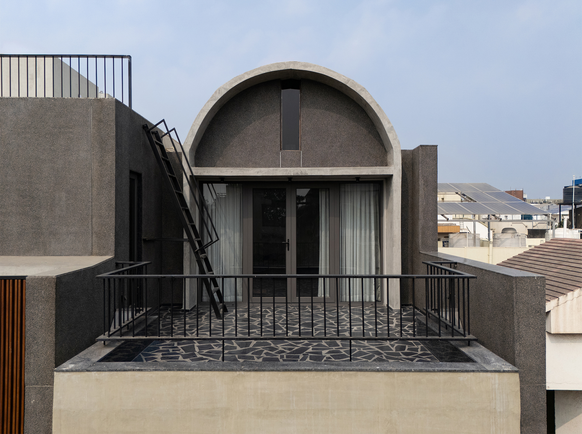 Exterior view of arched rooftop volume with mosaic terrace and black metal railings overlooking adjacent buildings
