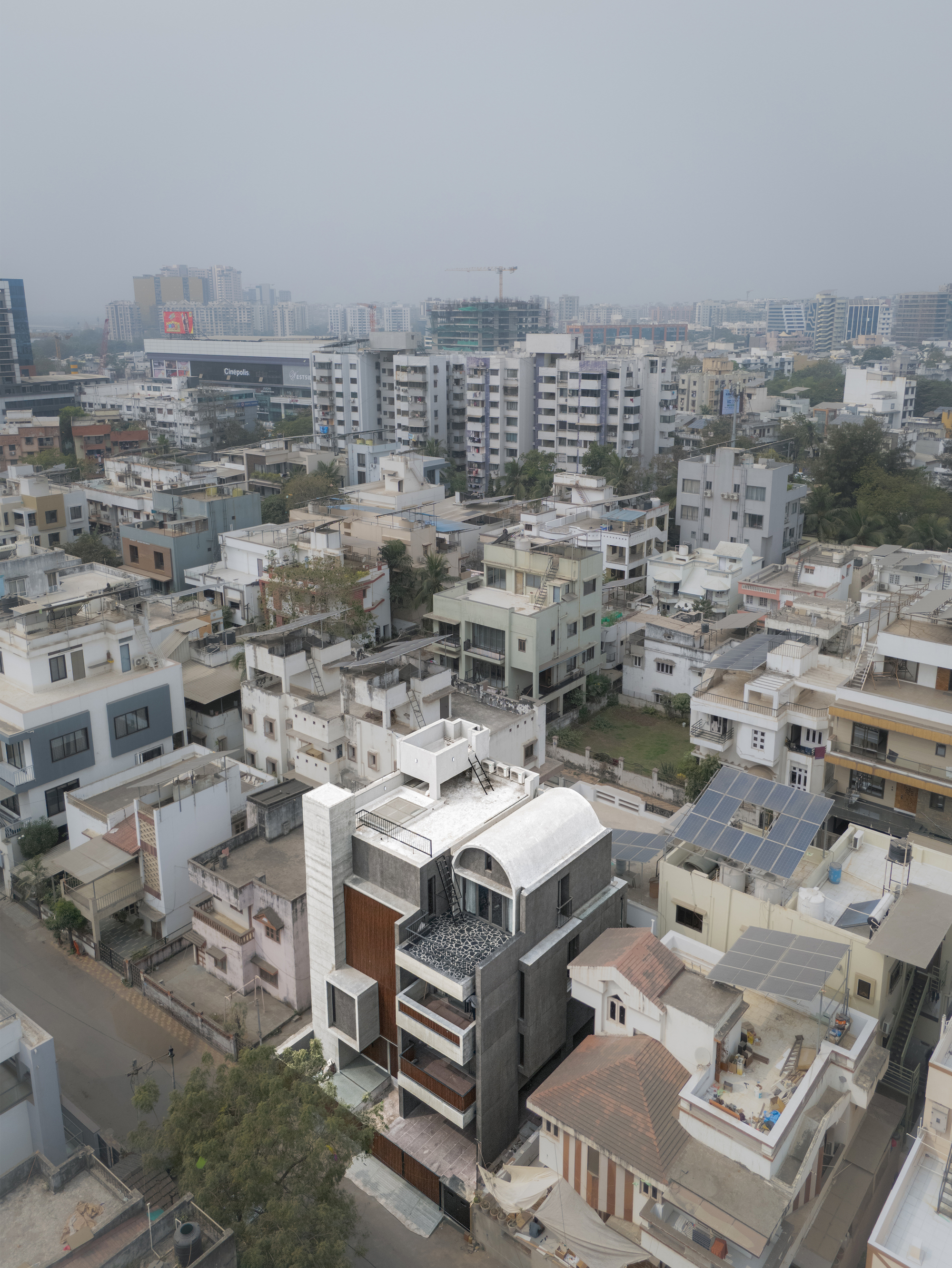 Aerial view of the multi-storey residence with curved roof volumes surrounded by dense urban fabric under overcast skies