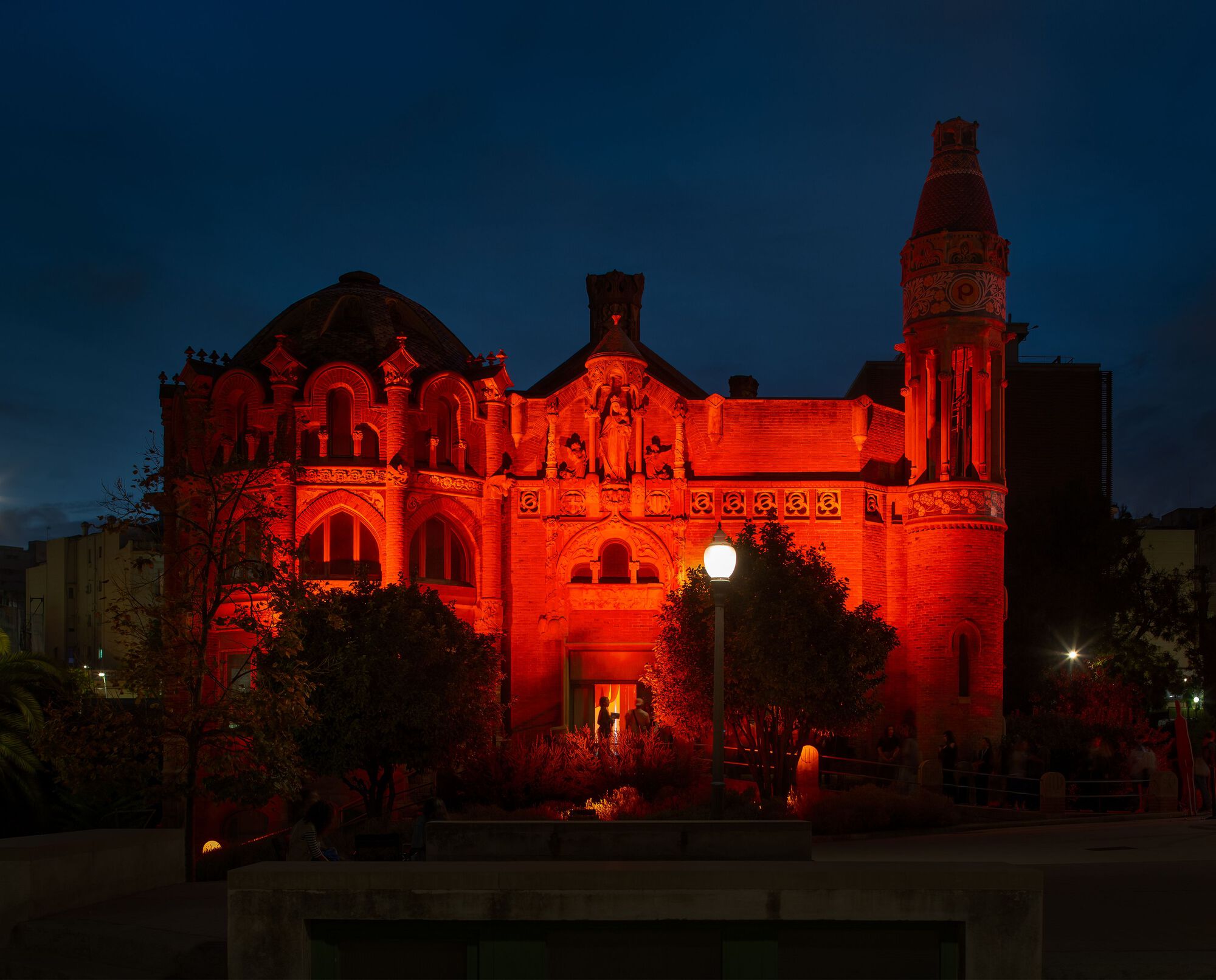 Historic brick building illuminated in red light at dusk with clock tower and arched entrance visible
