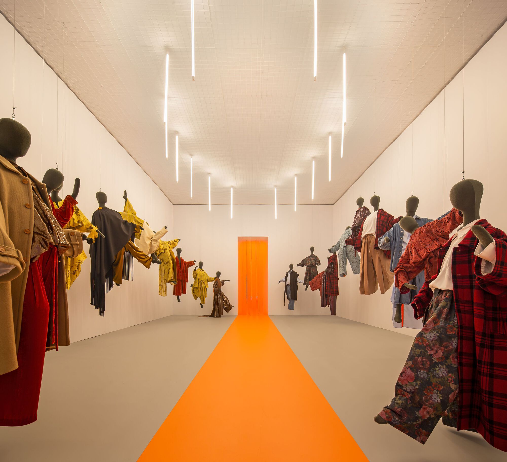 Long view of the exhibition hall with wall-mounted textile displays and vertical tube lighting in the ceiling