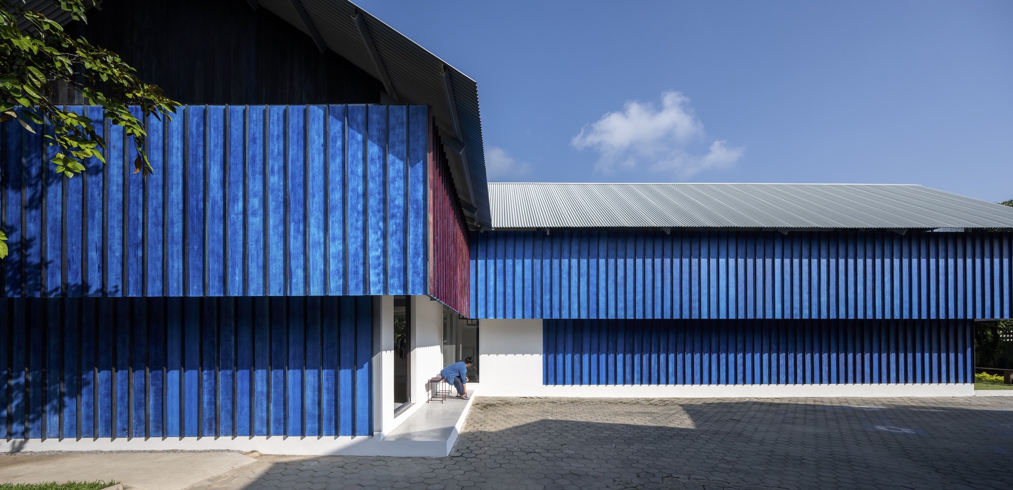 Street view of the blue corrugated metal facade with recessed entrance under partly cloudy skies