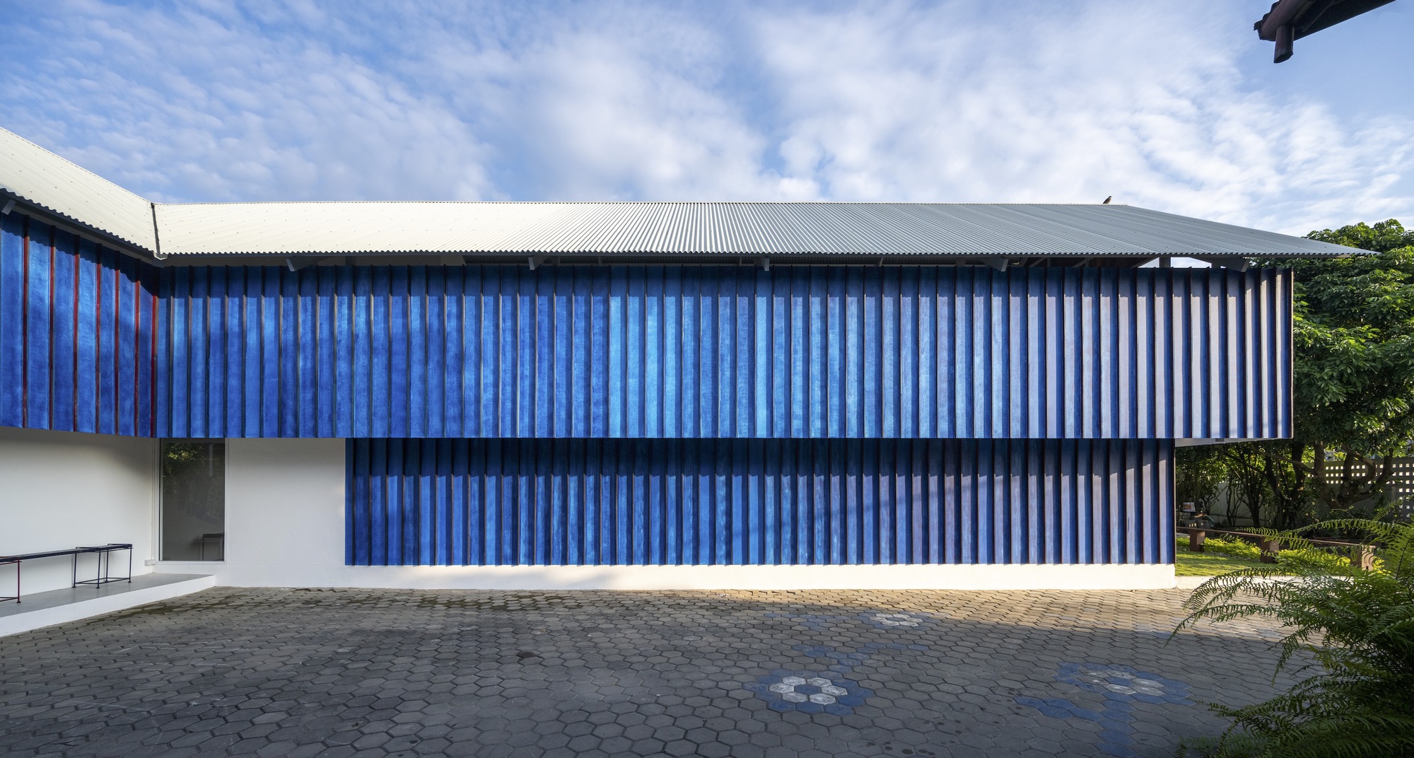 Long blue corrugated facade with horizontal banding and metal roof edge against cloudy sky