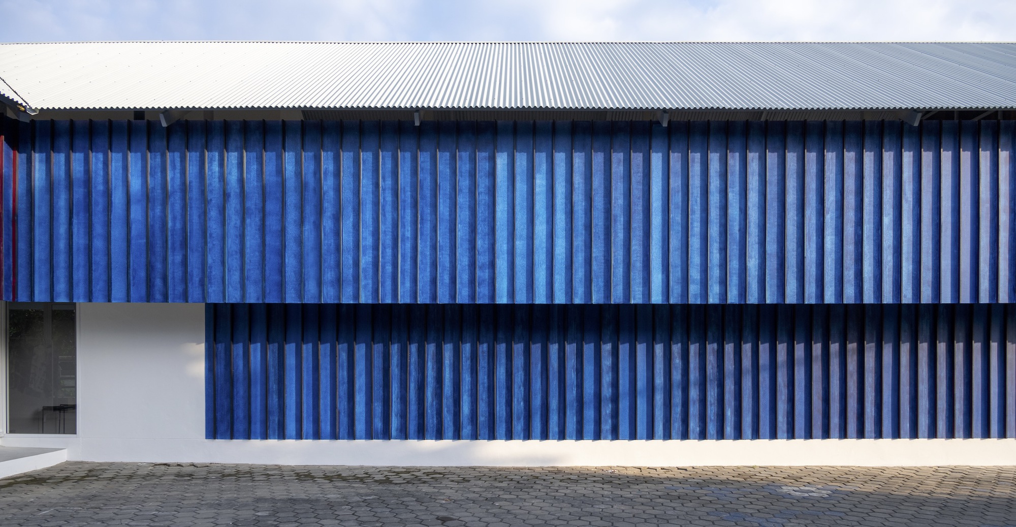 Street facade with vertical blue corrugated metal panels above a white base and corrugated metal roof