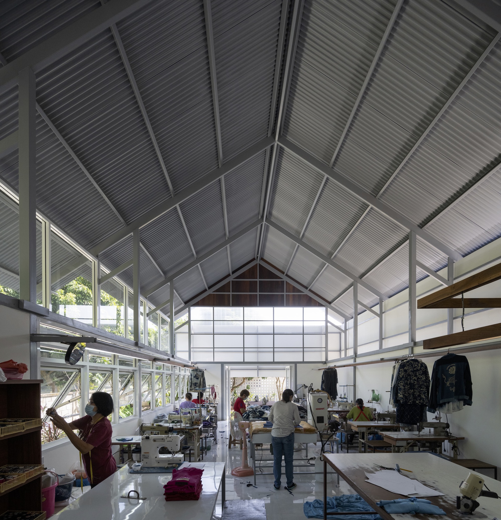 Workshop floor with sewing stations and workers under the steel-framed gabled ceiling with corrugated cladding