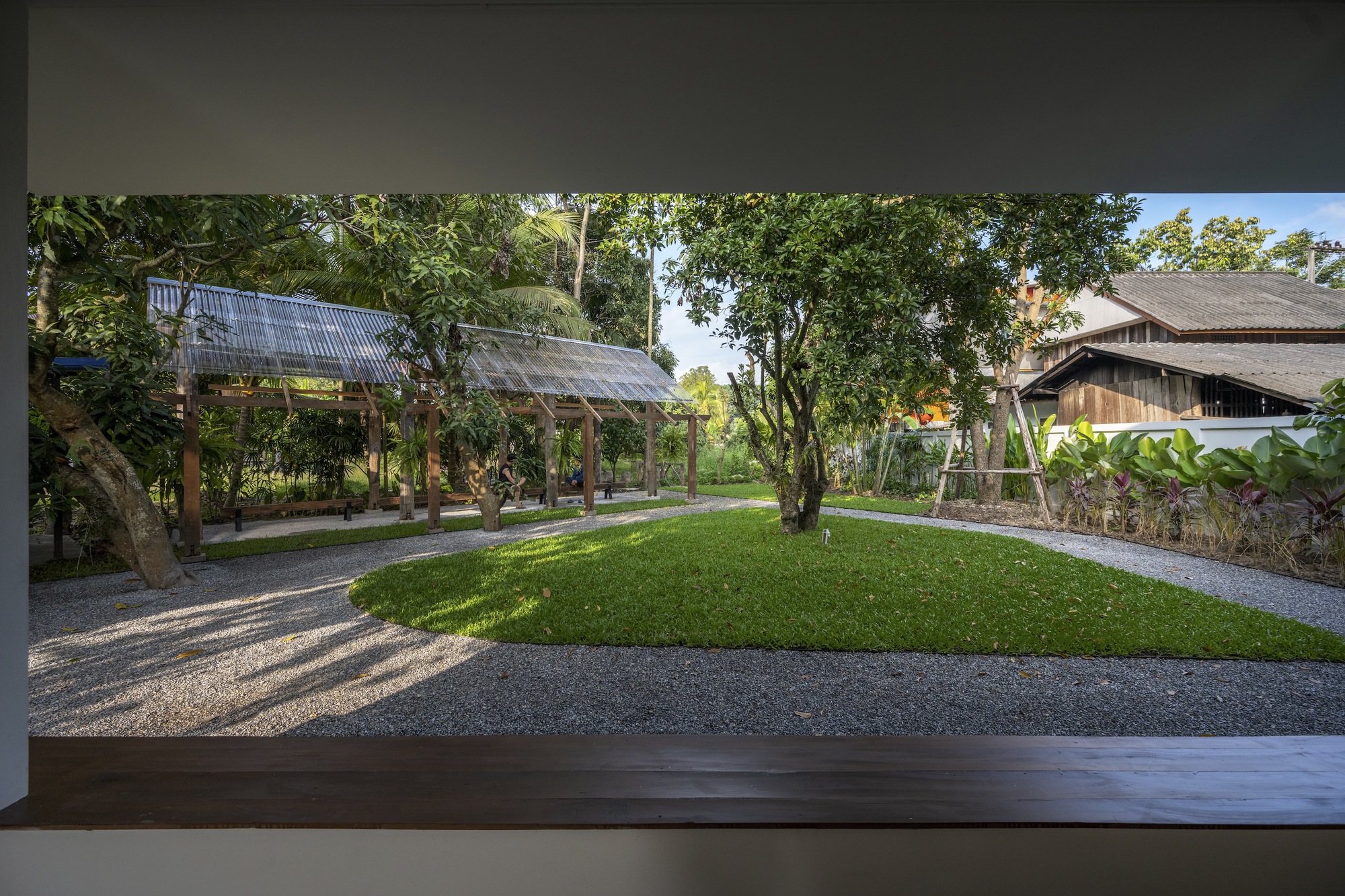 Framed view from interior to the garden courtyard with lawn, gravel paths, and timber pavilion structures