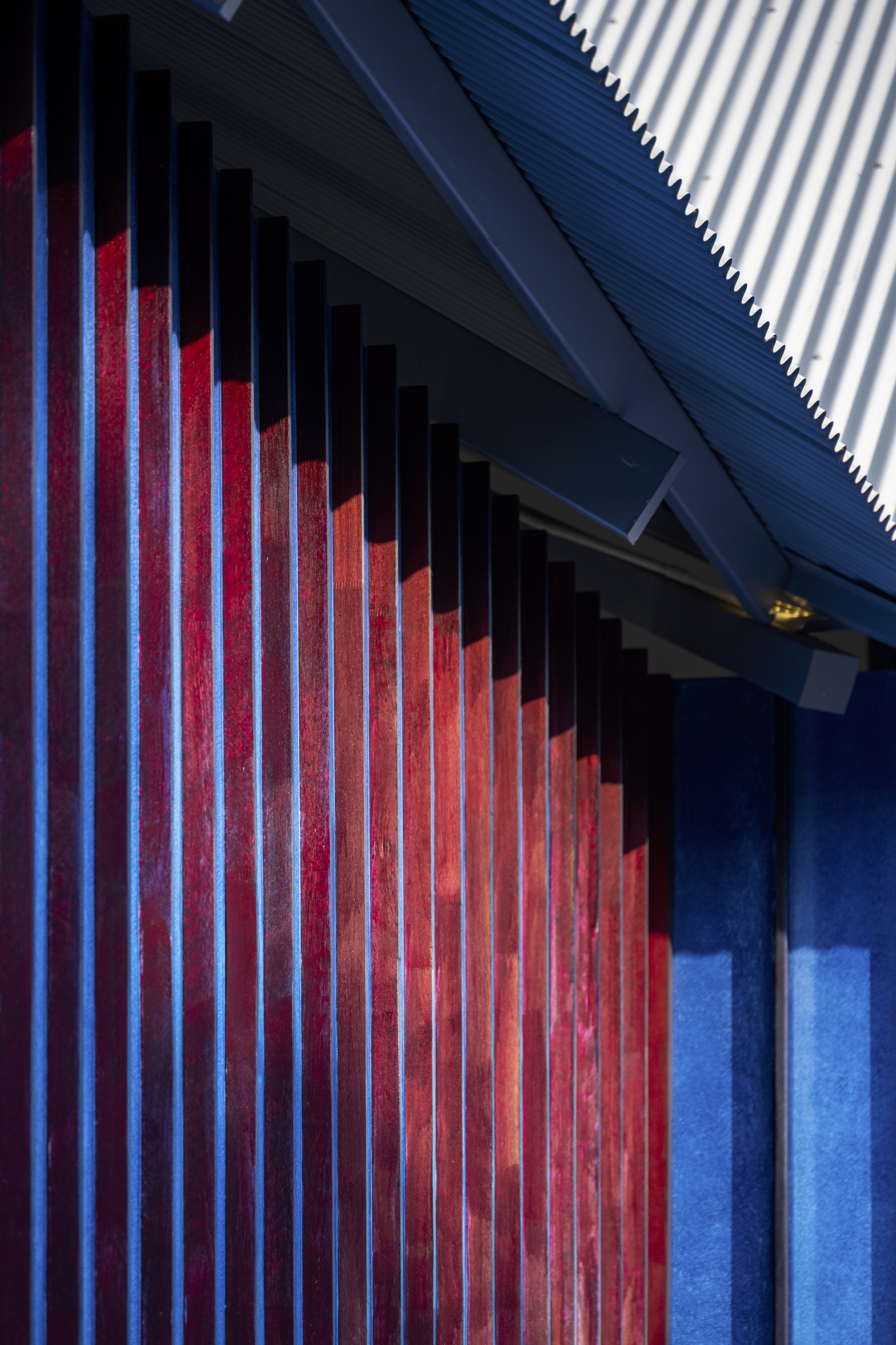 Red vertical timber slats against a corrugated metal soffit at dusk