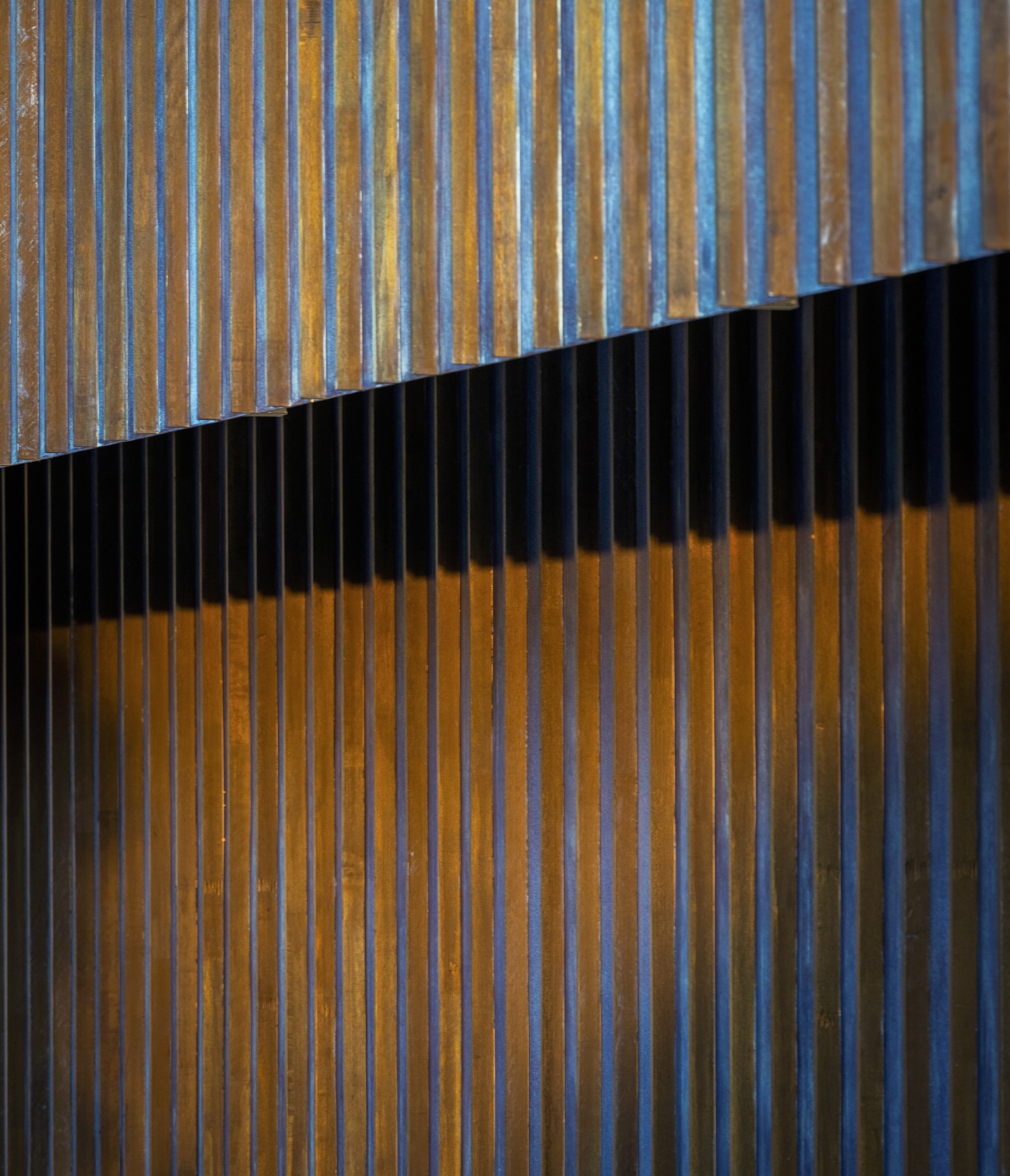 Diagonal metal screen casting shadows across vertical timber slats in afternoon light