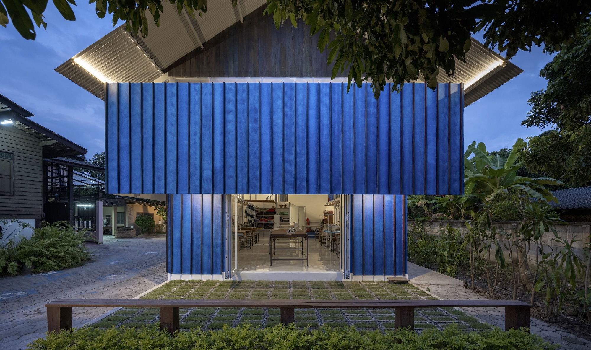 Blue corrugated facade with central glazed opening and timber bench at dusk