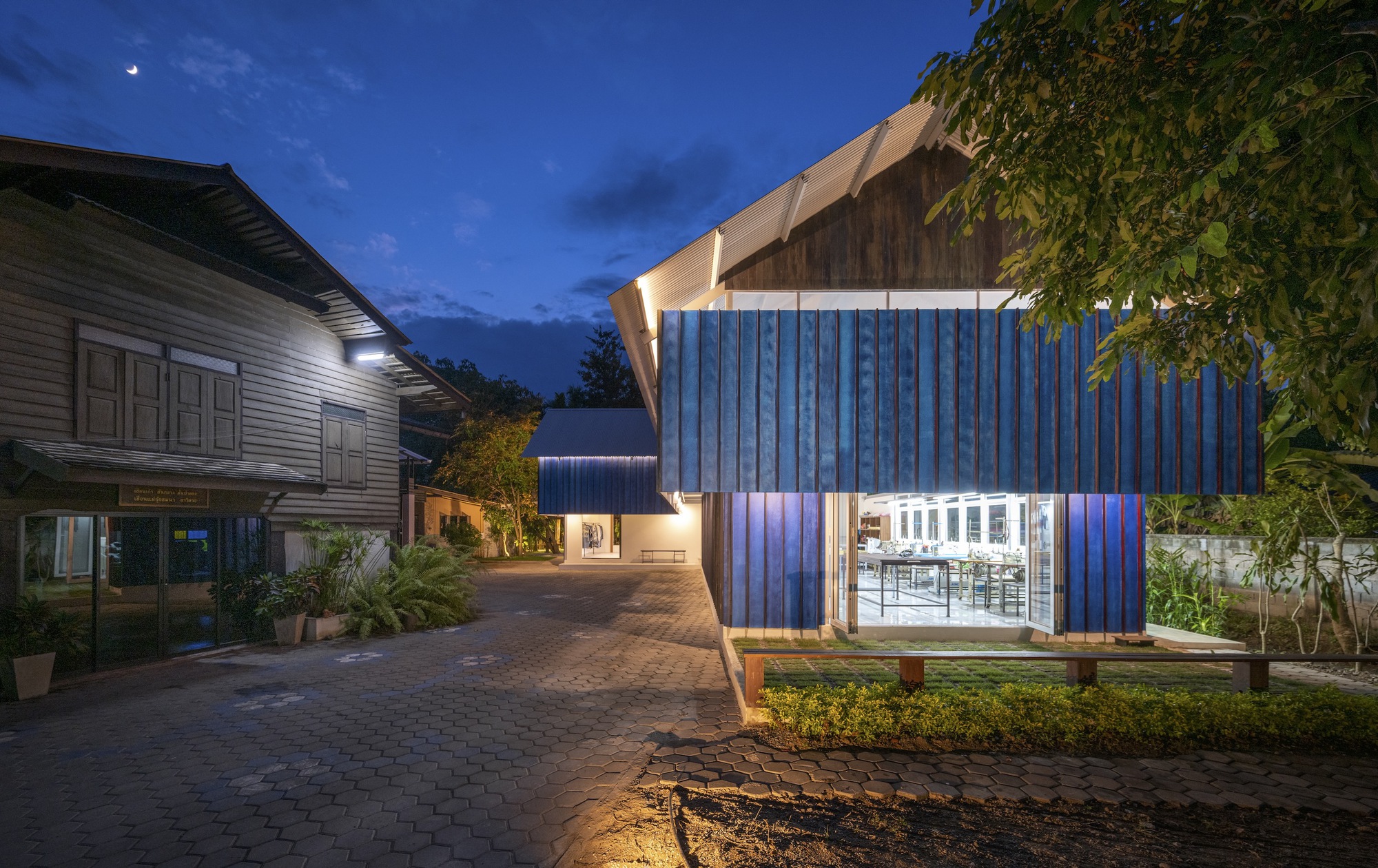 Illuminated pavilion with ribbed blue walls and upswept roof under evening sky