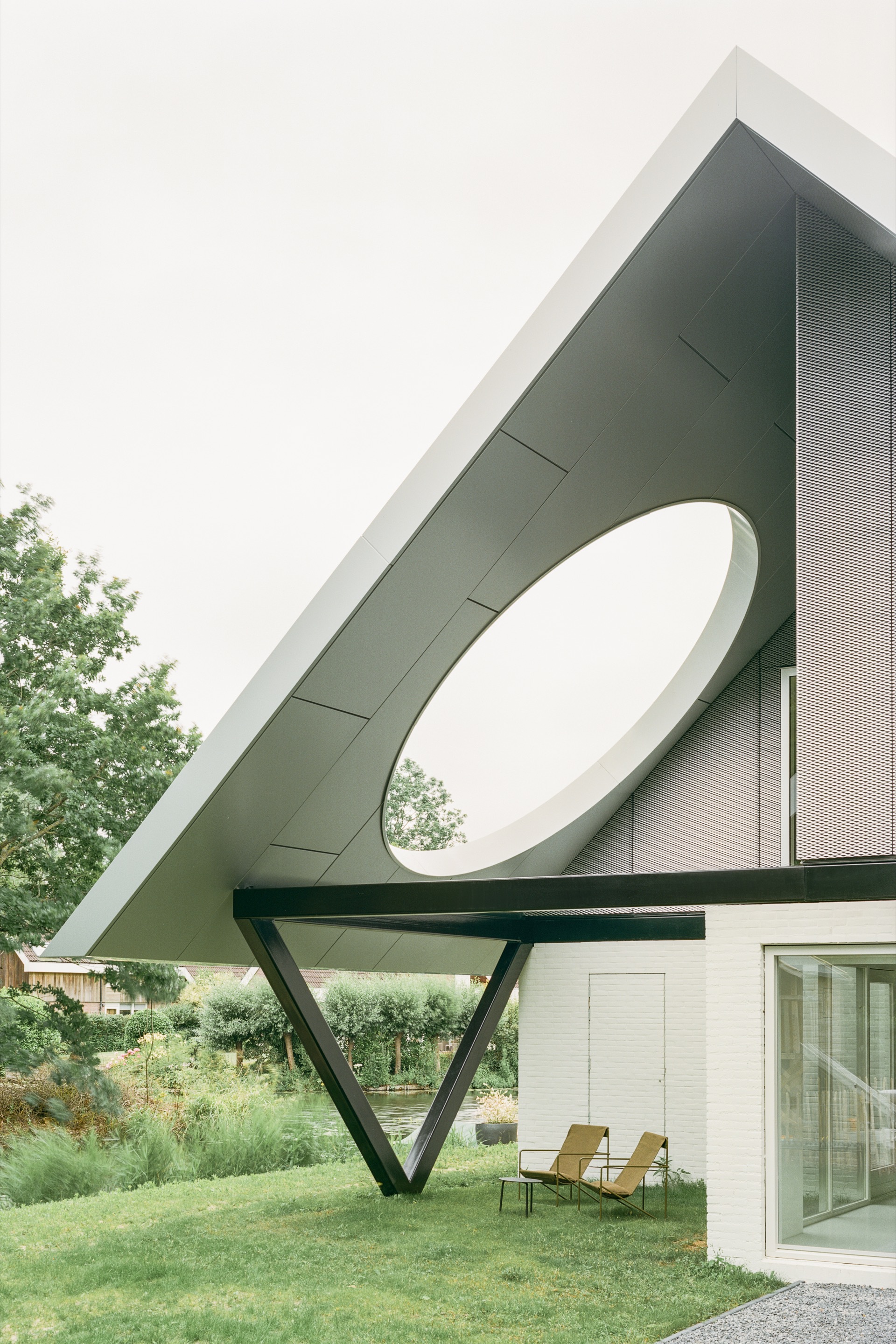 Perforated metal roof canopy with circular aperture and angled steel support over terrace