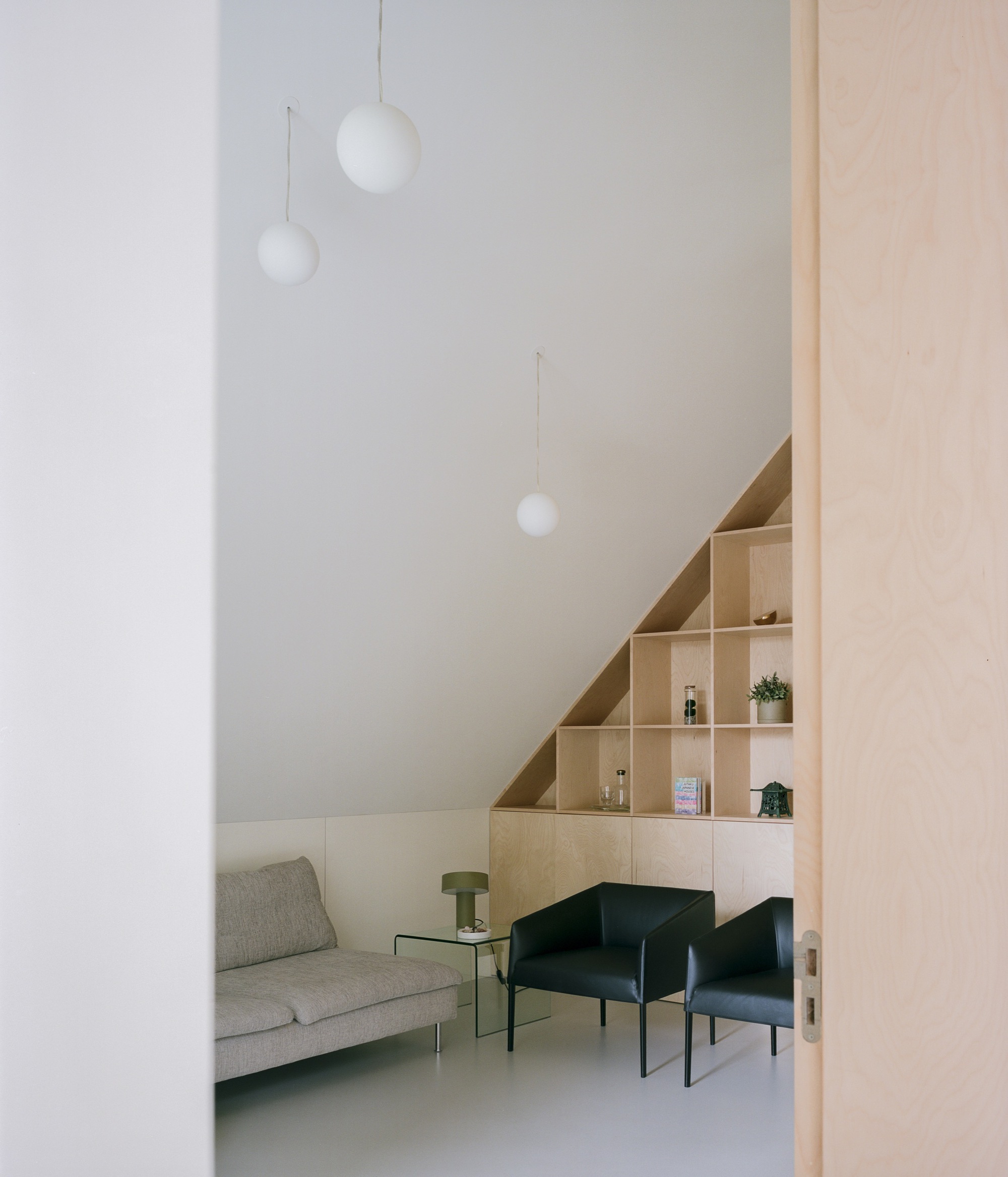 Interior view through doorway showing plywood shelving under pitched ceiling with pendant lights