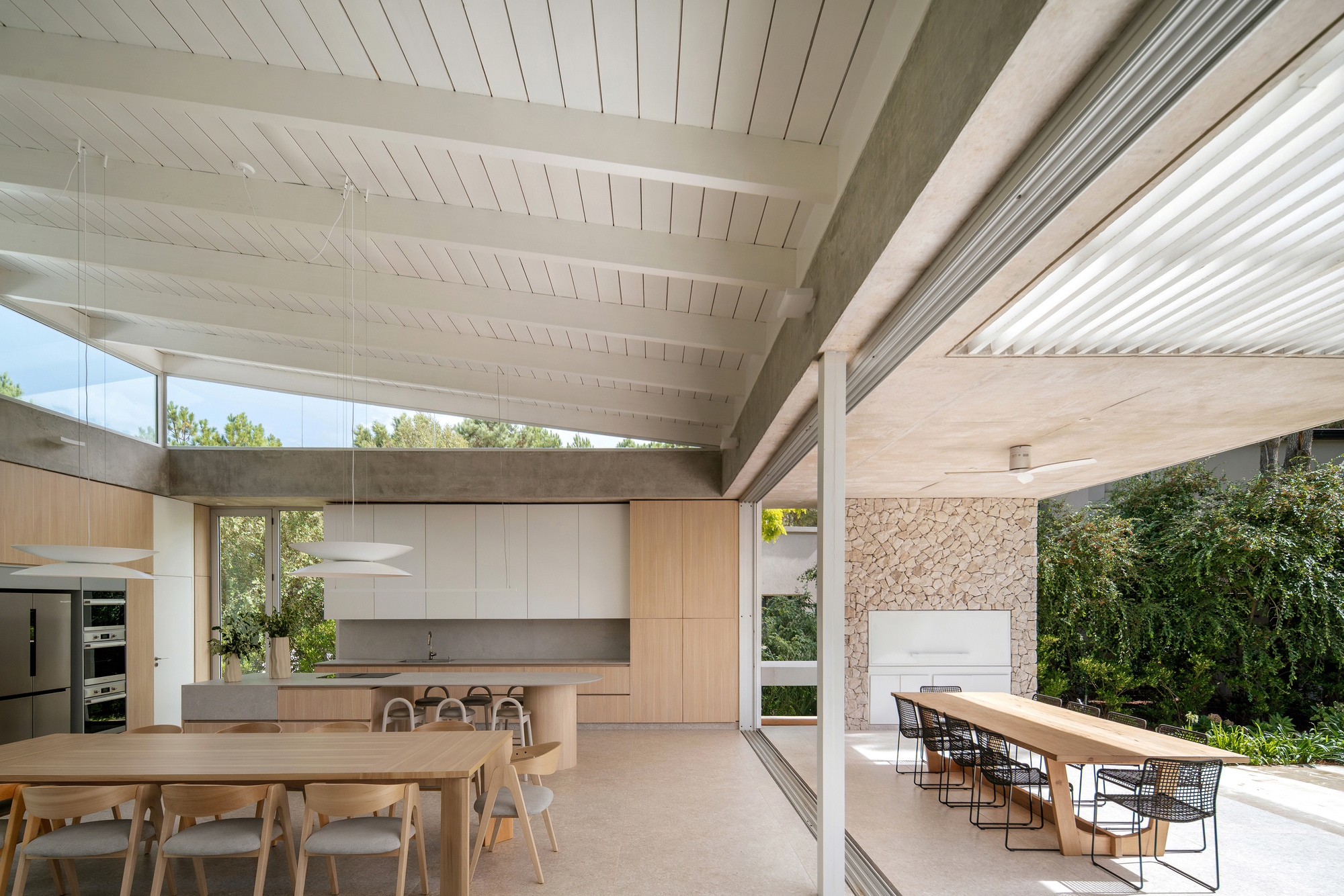 Open-plan kitchen and dining area with white timber ceiling and full-height glazing to the garden