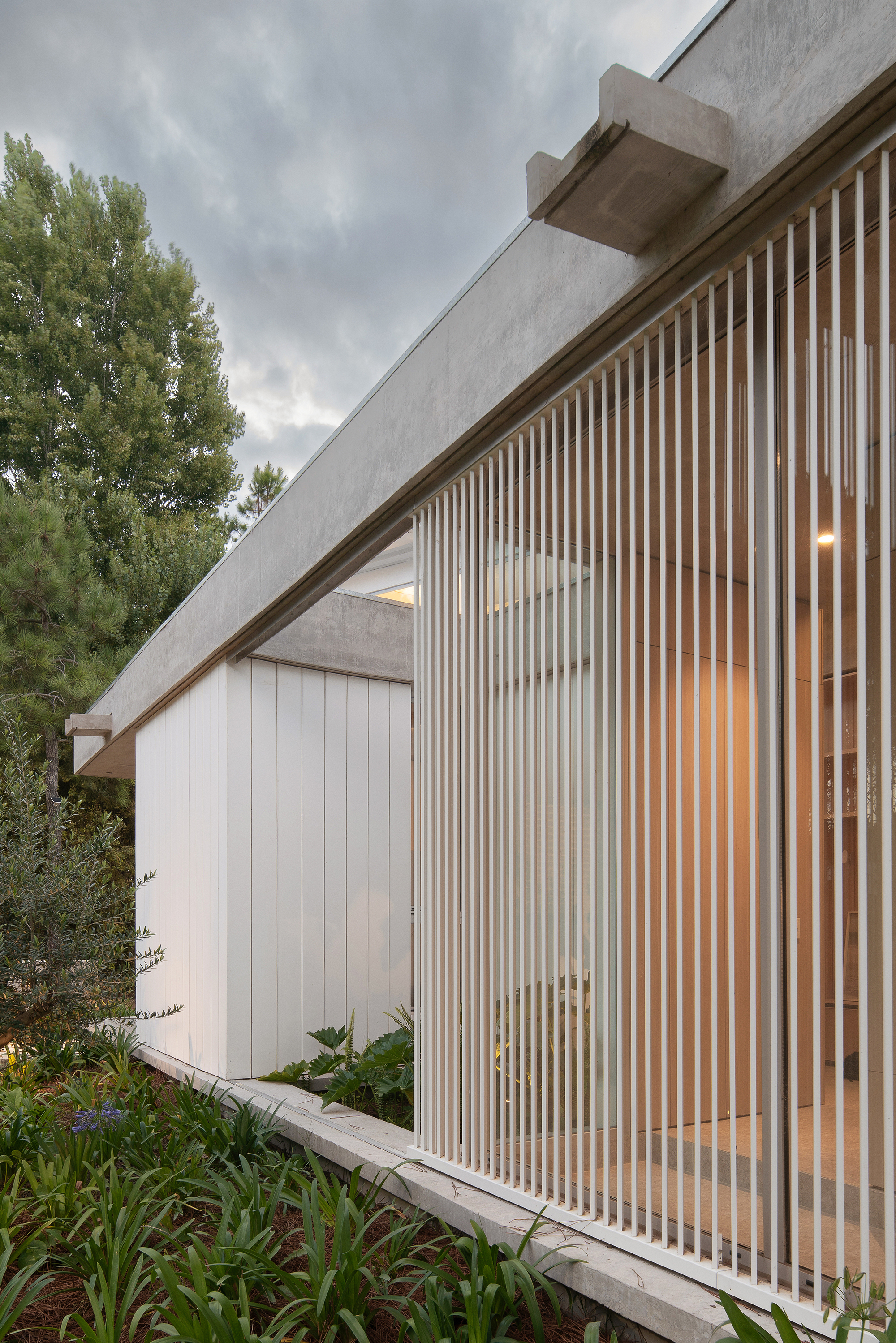 Angled facade with vertical timber battens over glazing and white cladding under a cloudy sky